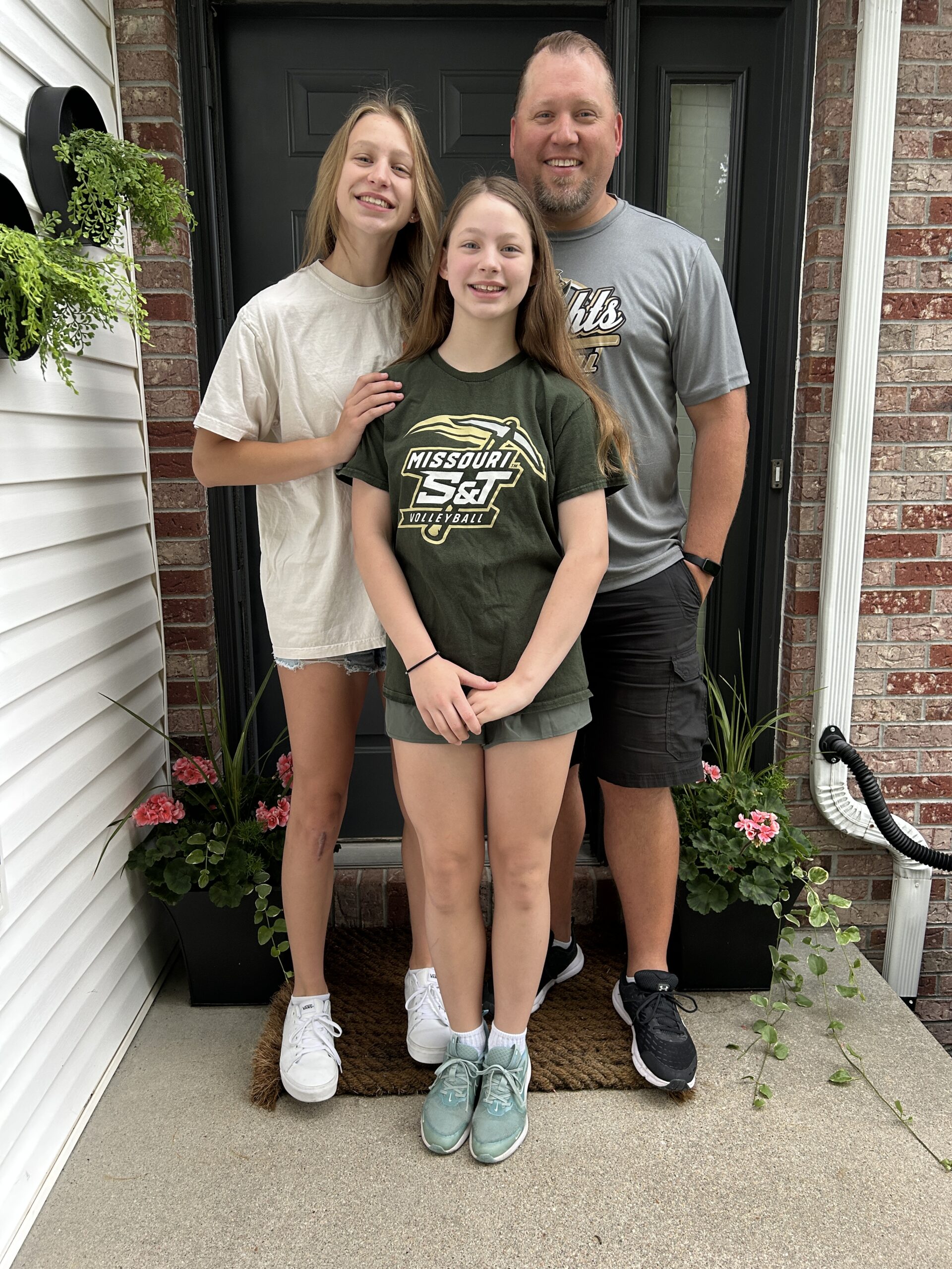 Last day of school photos on the porch with sisters hugging and smiling and dad who is a teacher in the photo too