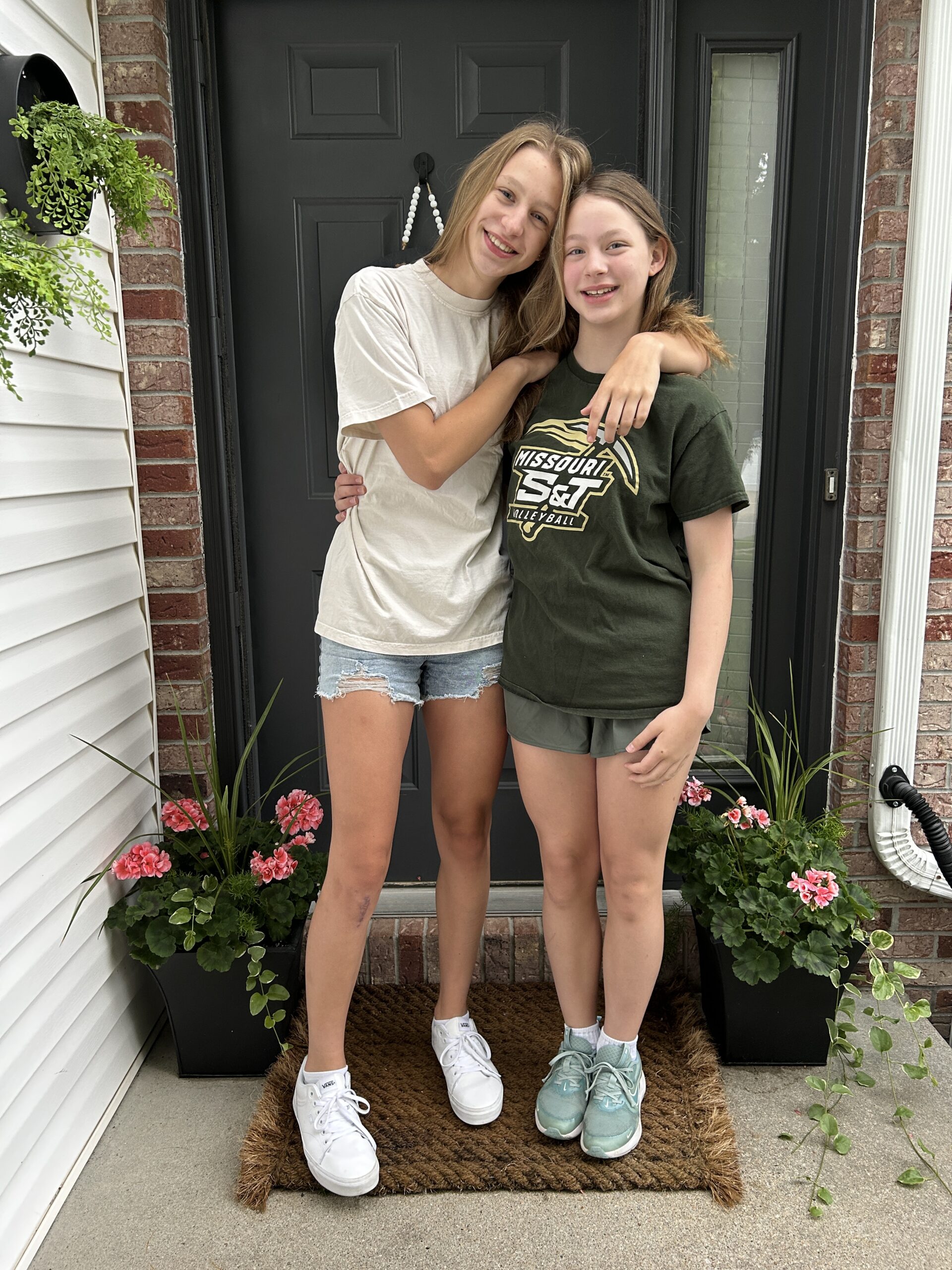 Last day of school photos on the porch with sisters hugging and smiling