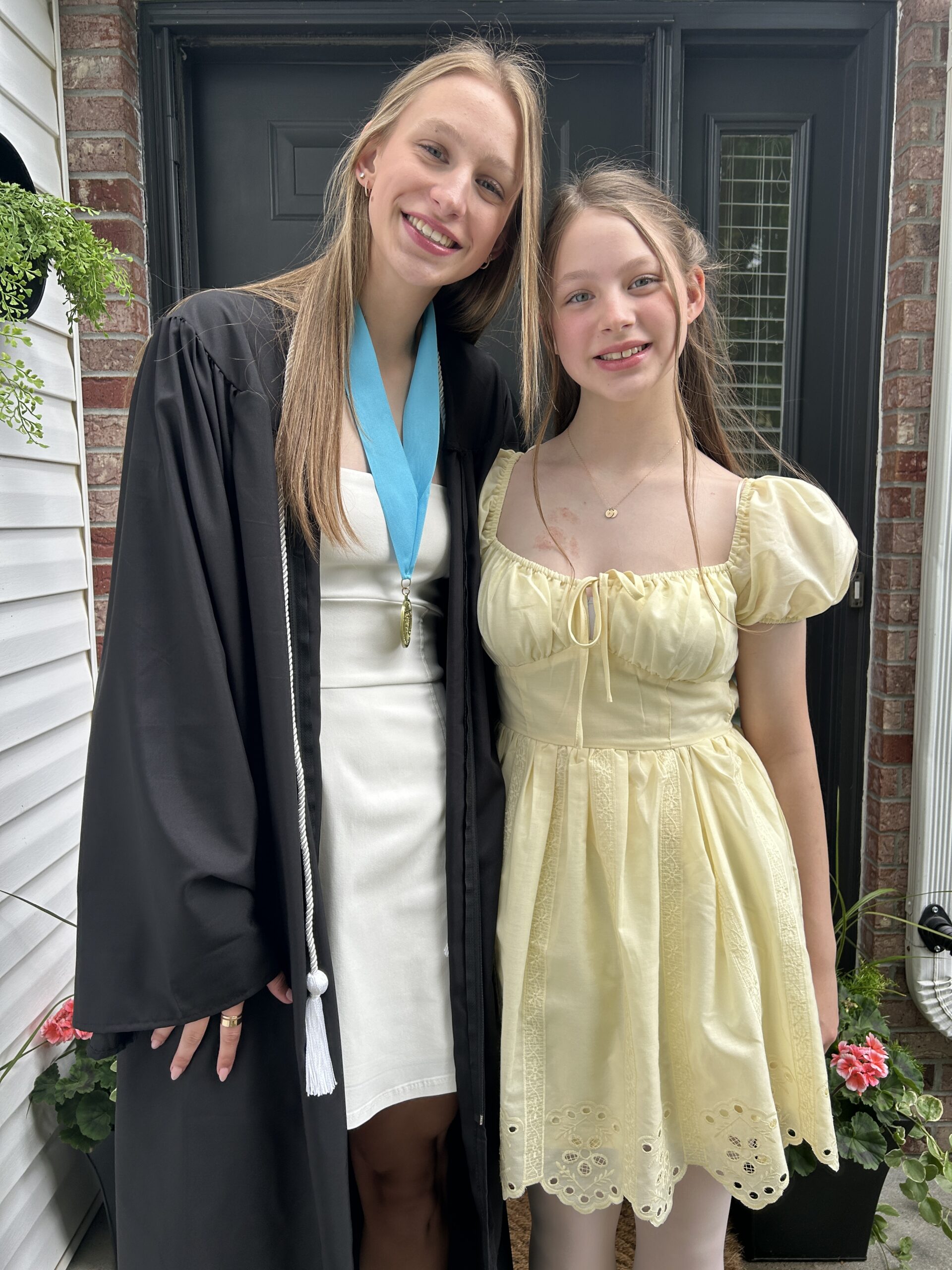 Sisters taking a photow with the older sister in her cap and gown for graduation
