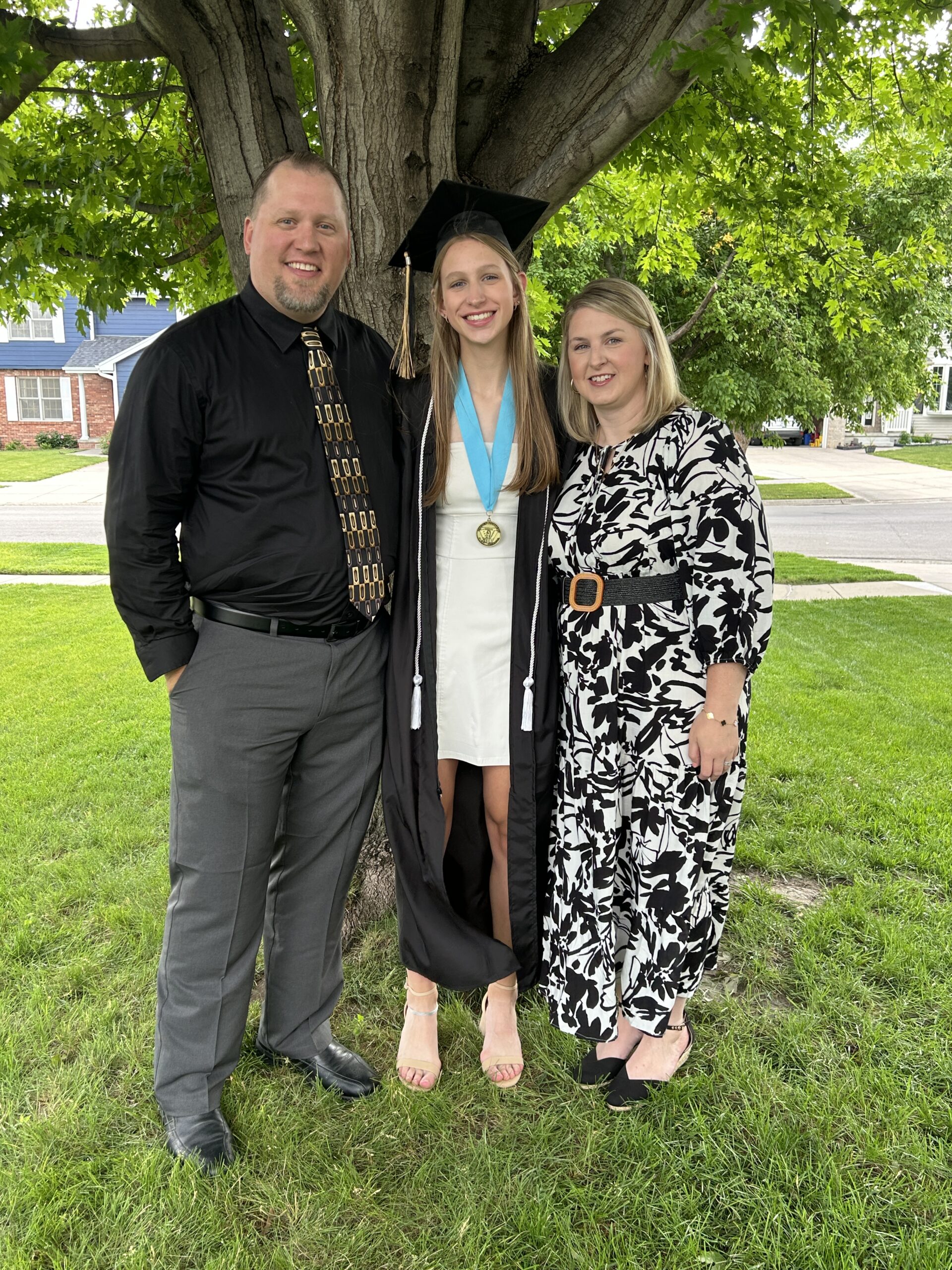 Parents standing and smiling with their daughter in her cap and gown and posing for picturtes