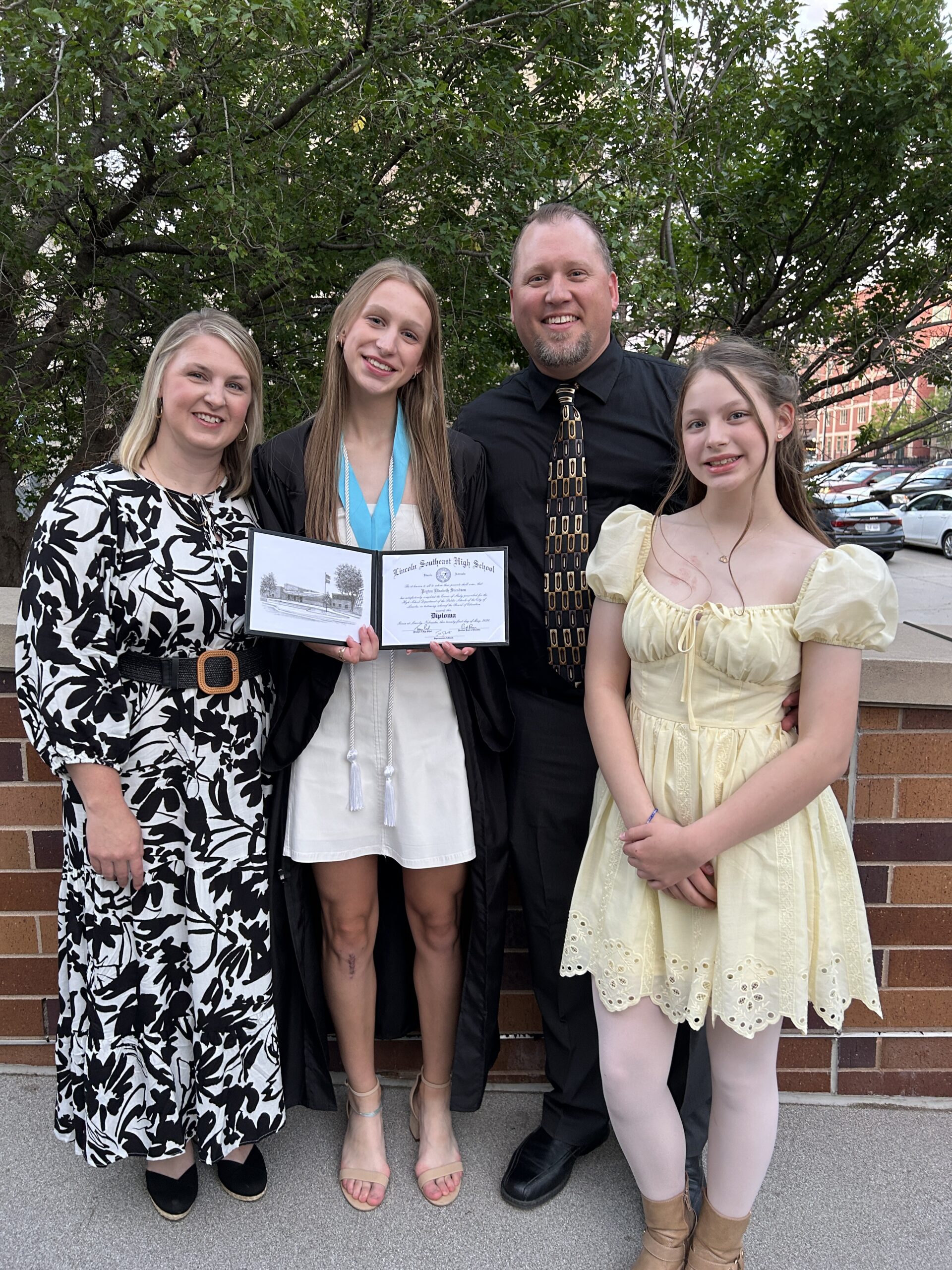 Family of four standing and smiling for a photo after the oldest daughter's graduation