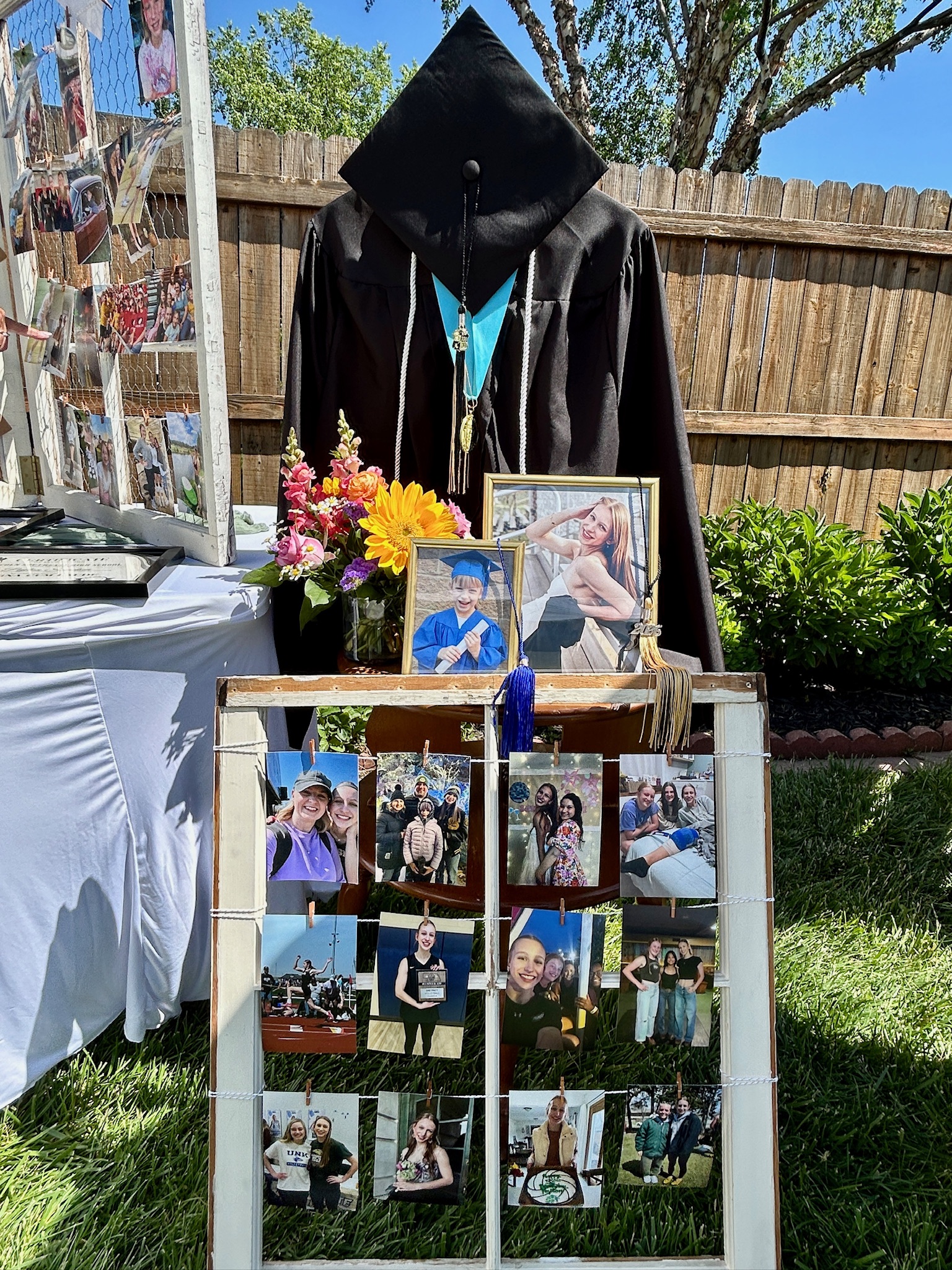 Graduation cap and gown display on a small side table with a colorful boquet and photos of the graduate from preschool and high school