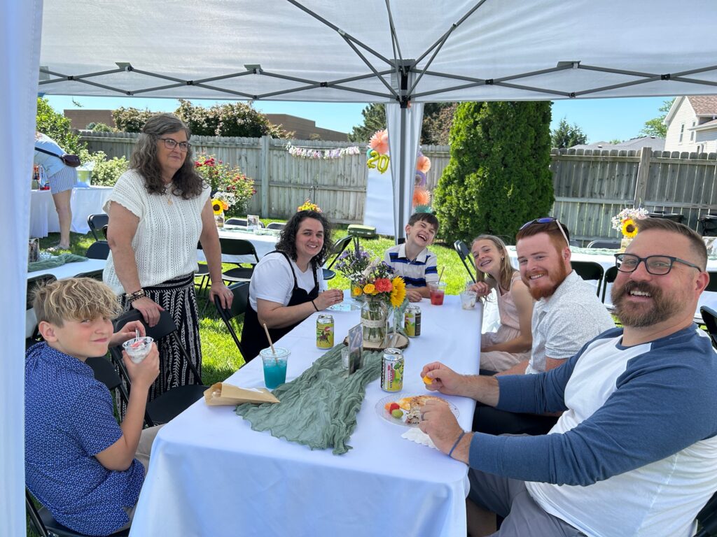 Family and friends gathered under a tent enjoying brunch and conversation at an outdoor high school graduation party.