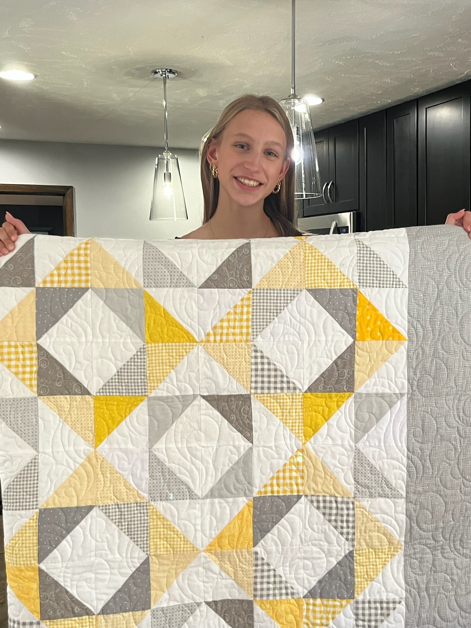Girl holding yellow, gray and white quilt custom-made for her by her great-grandmother as a graduation gift