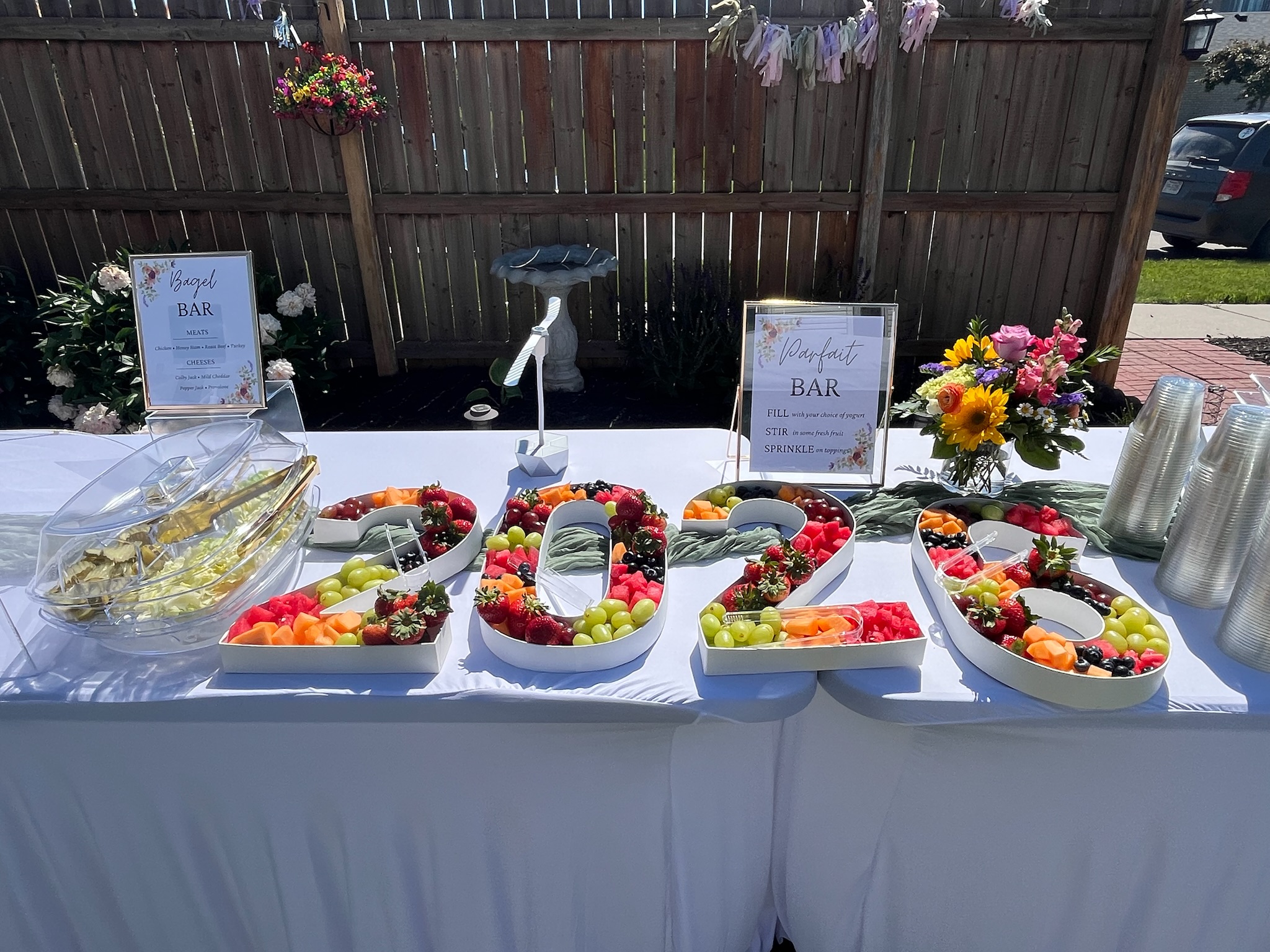 Graduation brunch parfait bar with fresh fruit tray, yogurt toppings, floral arrangements, and custom party signage.