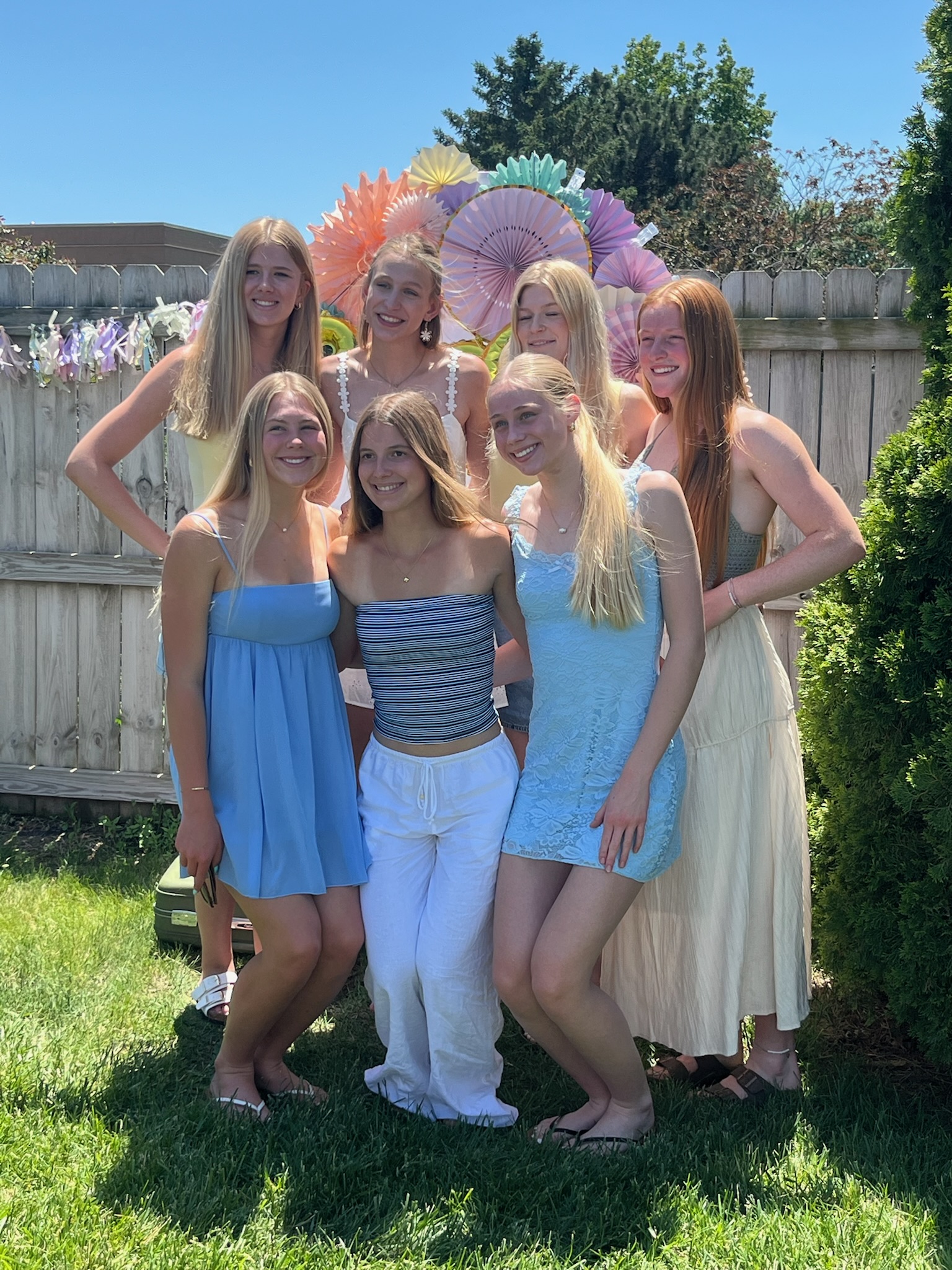 Group of friends posing together at an outdoor graduation party in front of a pastel paper fan backdrop.