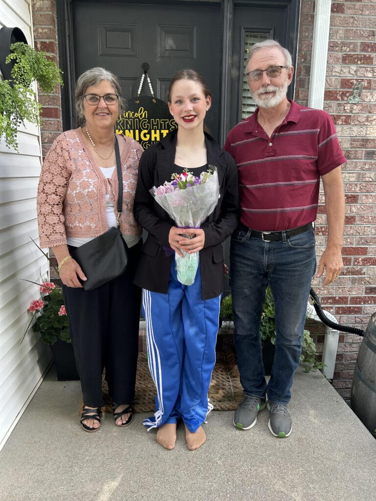 Grandparents standing with granddaughter while she holds a bouquet of flowers after performing at a dance recital