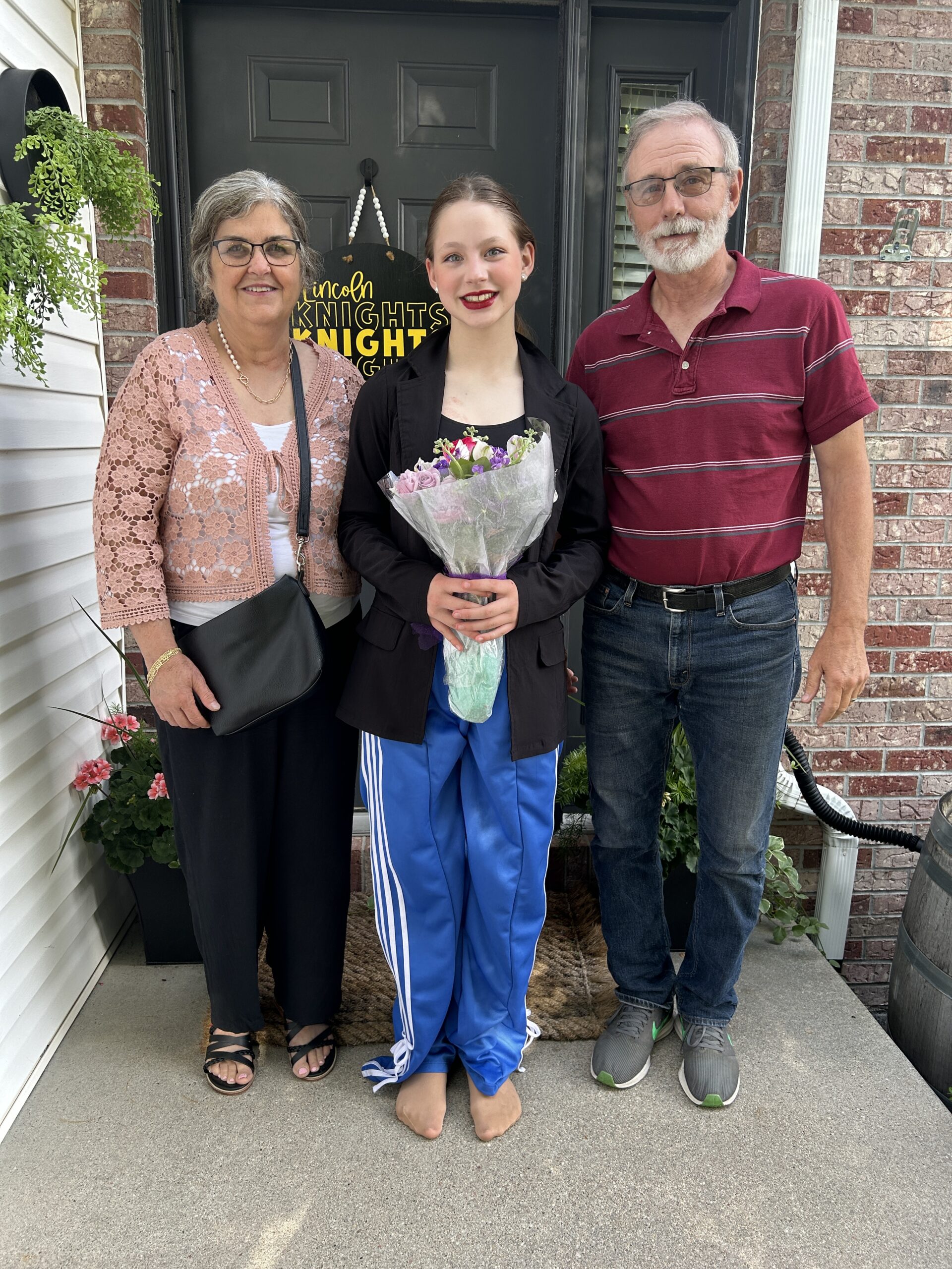 Grandparents standing with granddaughter while she holds a bouquet of flowers after performing at a dance recital