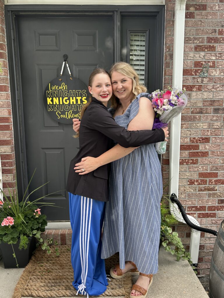 Mother and daughter smilinig and hugging while holding a bouquet of flowers after a dance recital