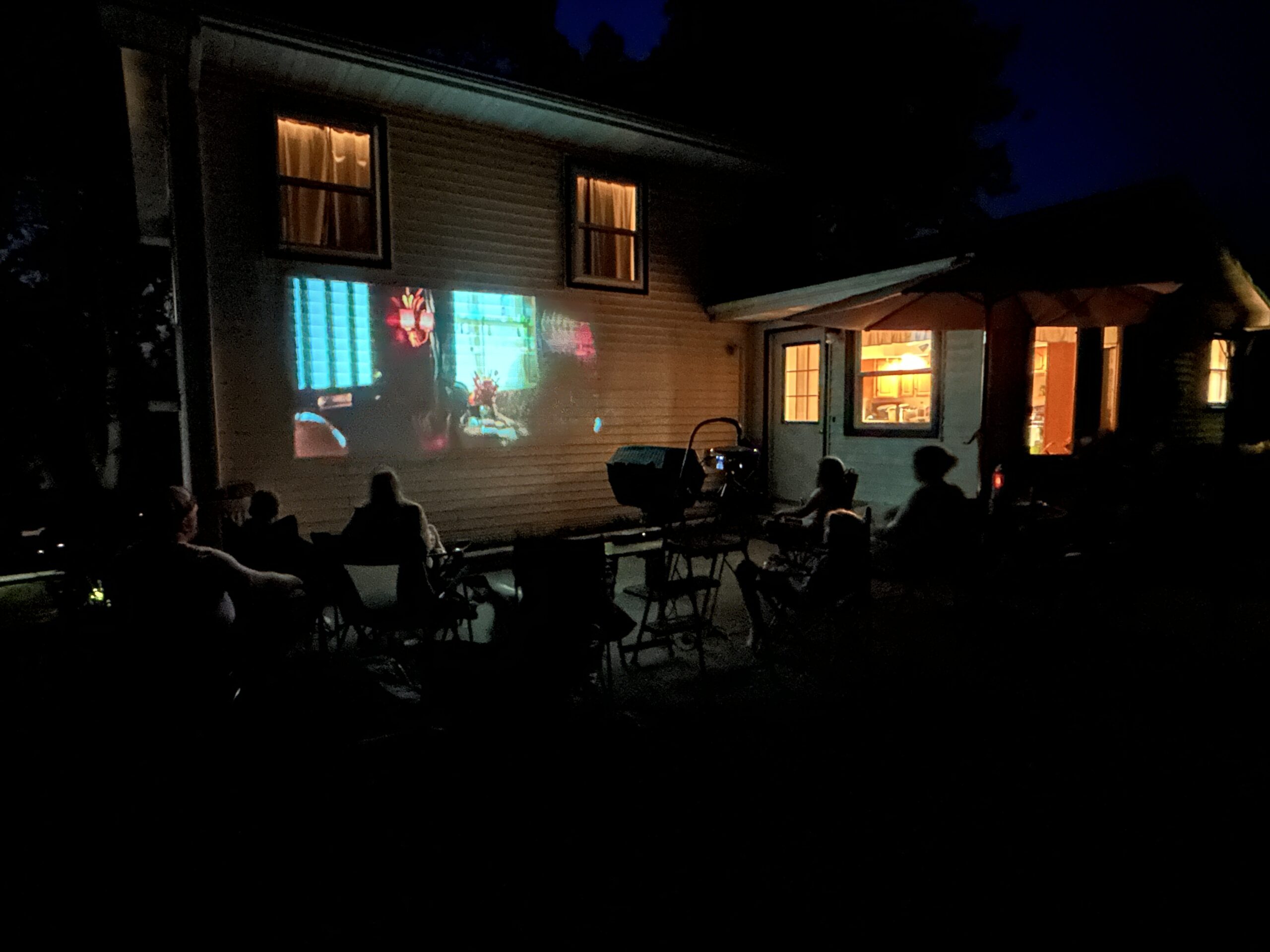 Outdoor movie night set up with a movie being projected on the back of a house