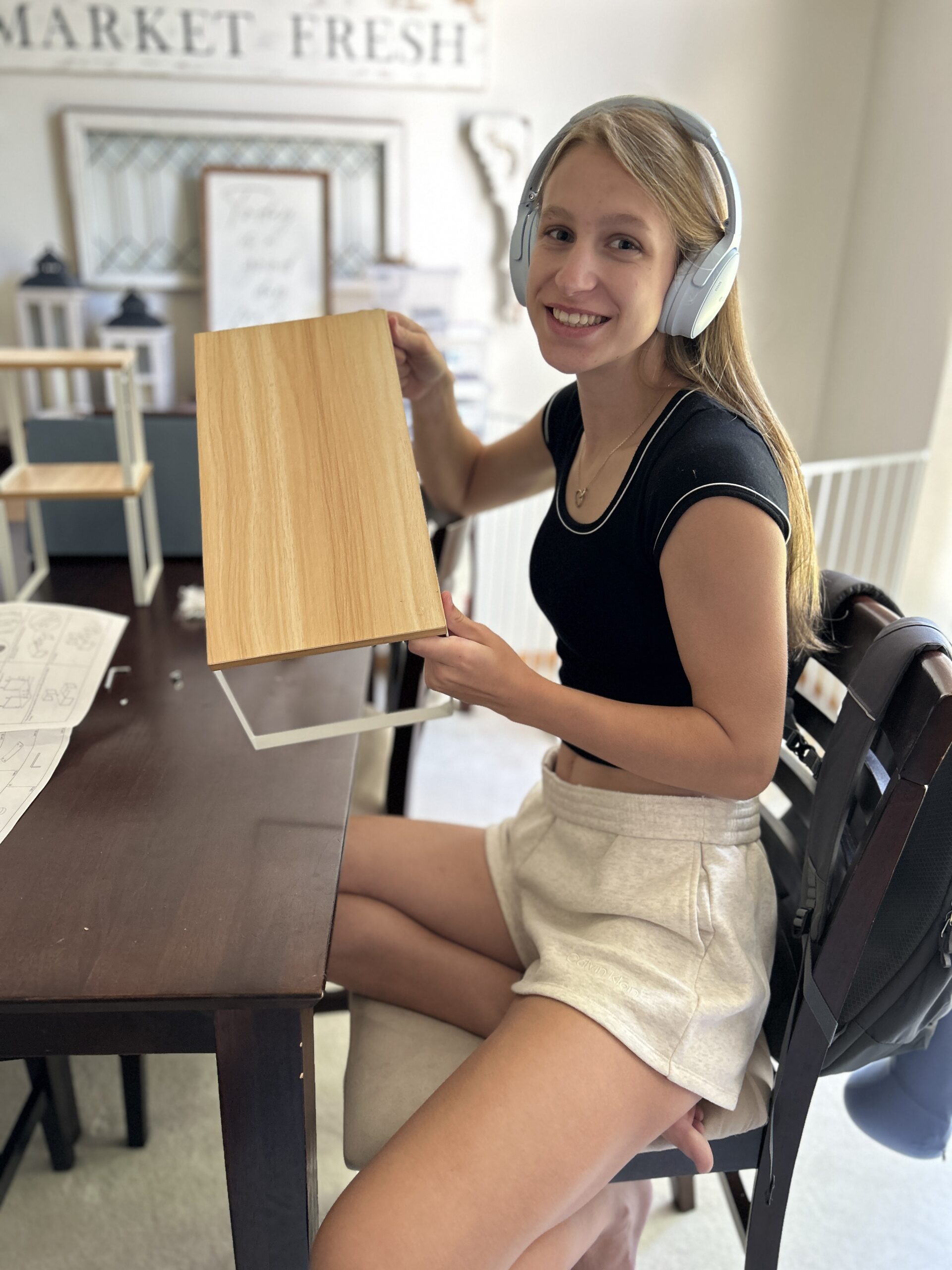 College student assembling dorm room furniture while wearing headphones at the dining room table.