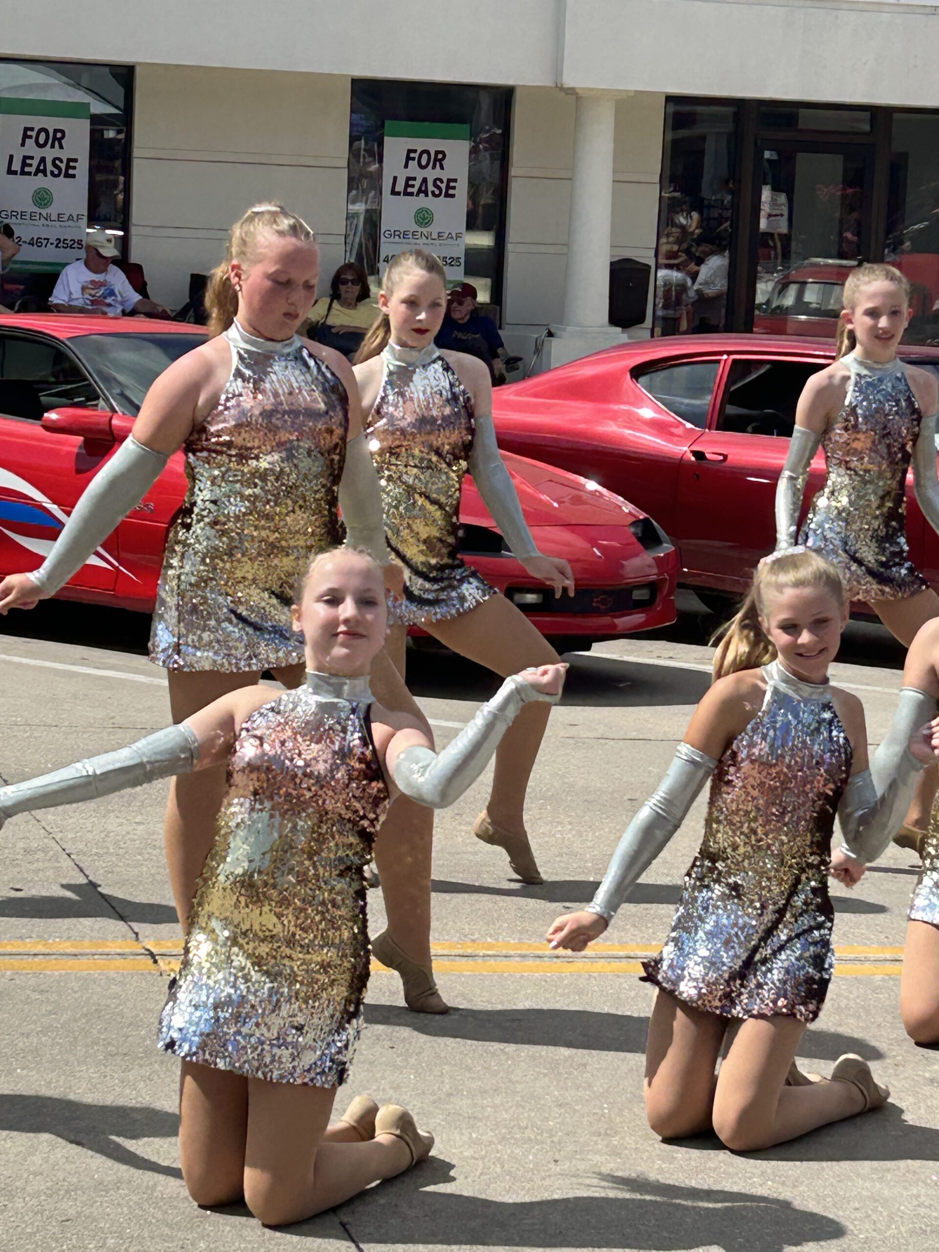 Dancers performing in sparkly silver costumes during a summer parade.