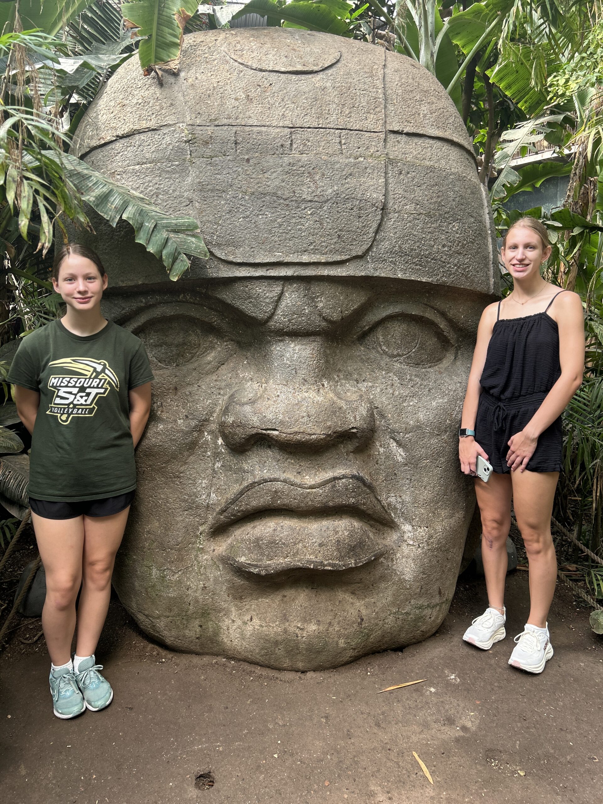 Two sisters posing beside a giant stone head sculpture inside the Henry Doorly Zoo in Omaha.