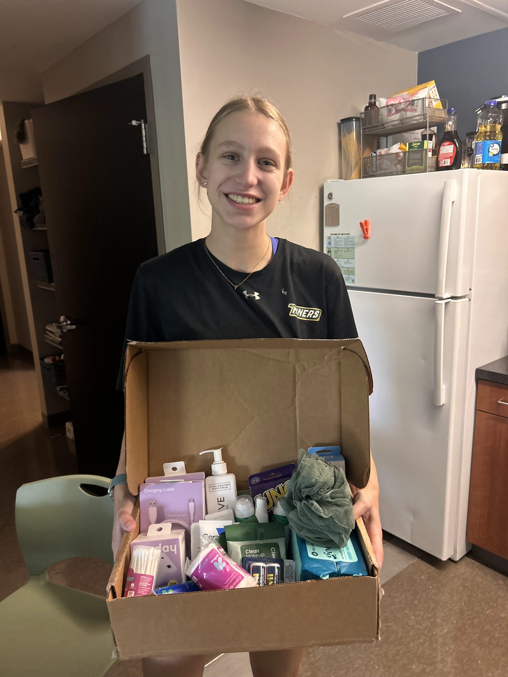 College student holding a care package filled with travel supplies and essentials for a college athlete.
