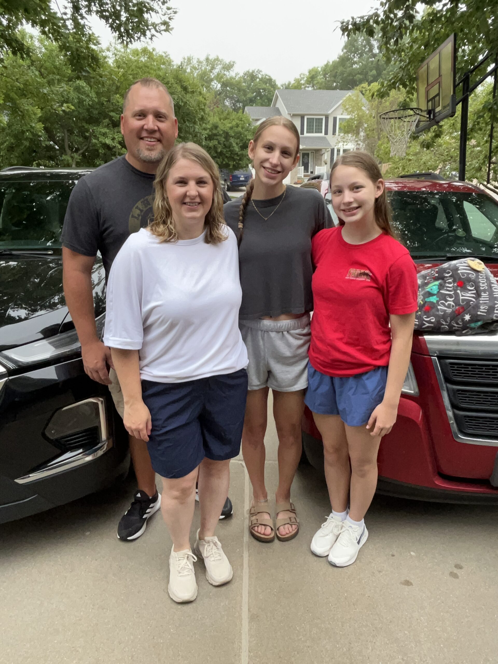 Family of four poses together between two packed vehicles before leaving for college move-in day.