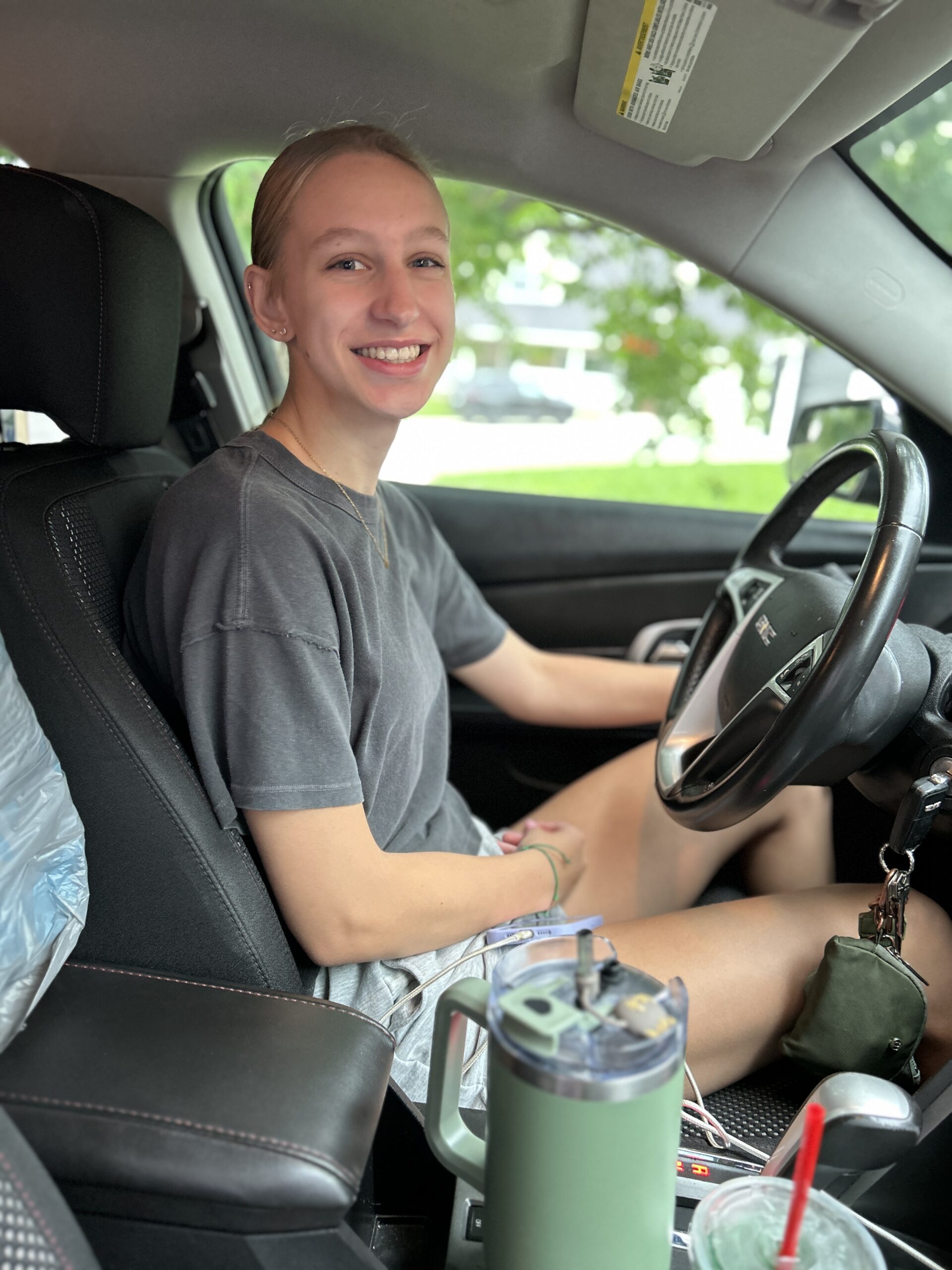 College student smiling in the driver’s seat of a car before leaving home for college.