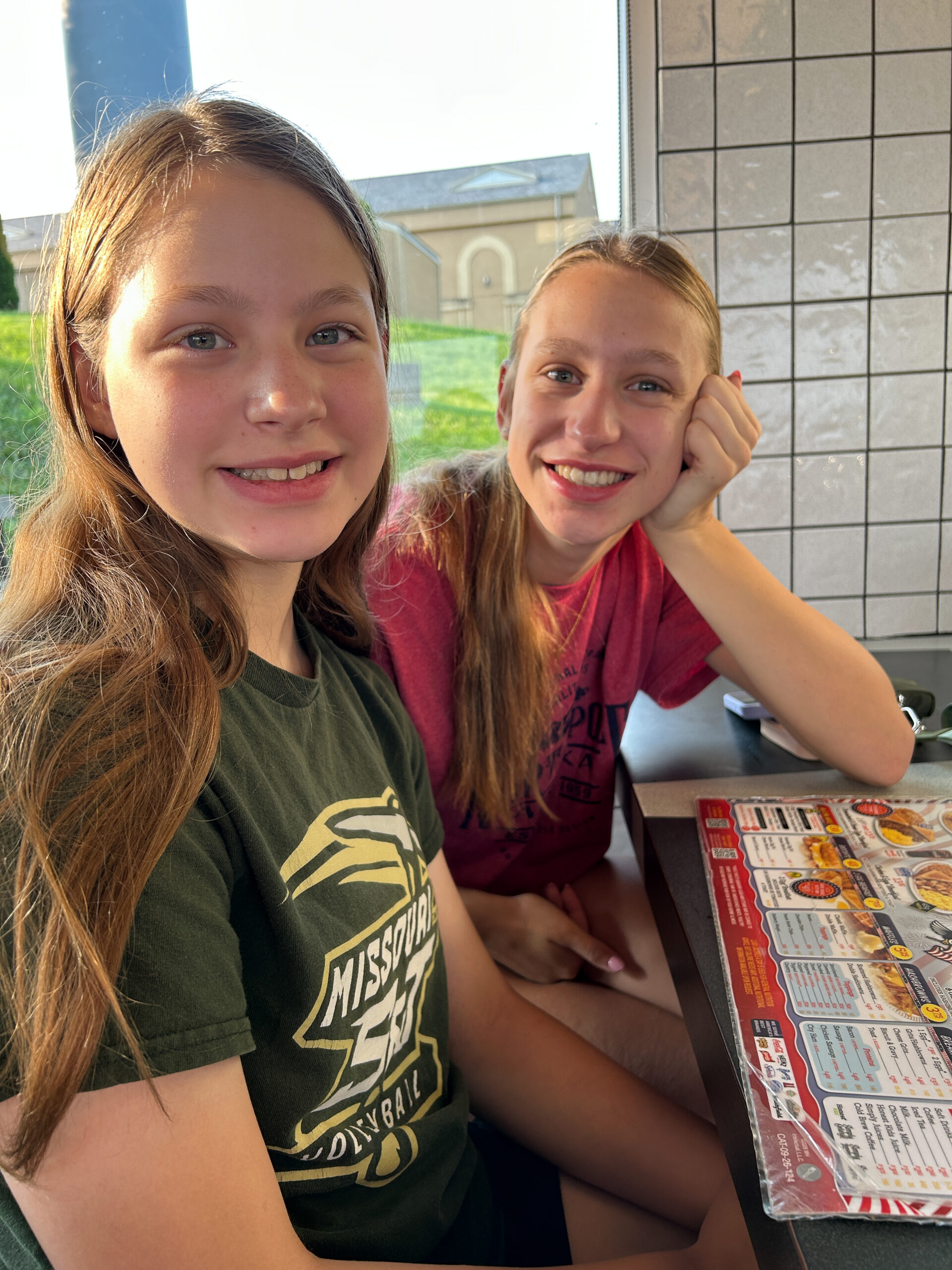 Two sisters smiling together while sitting at a restaurant during college move-in weekend.