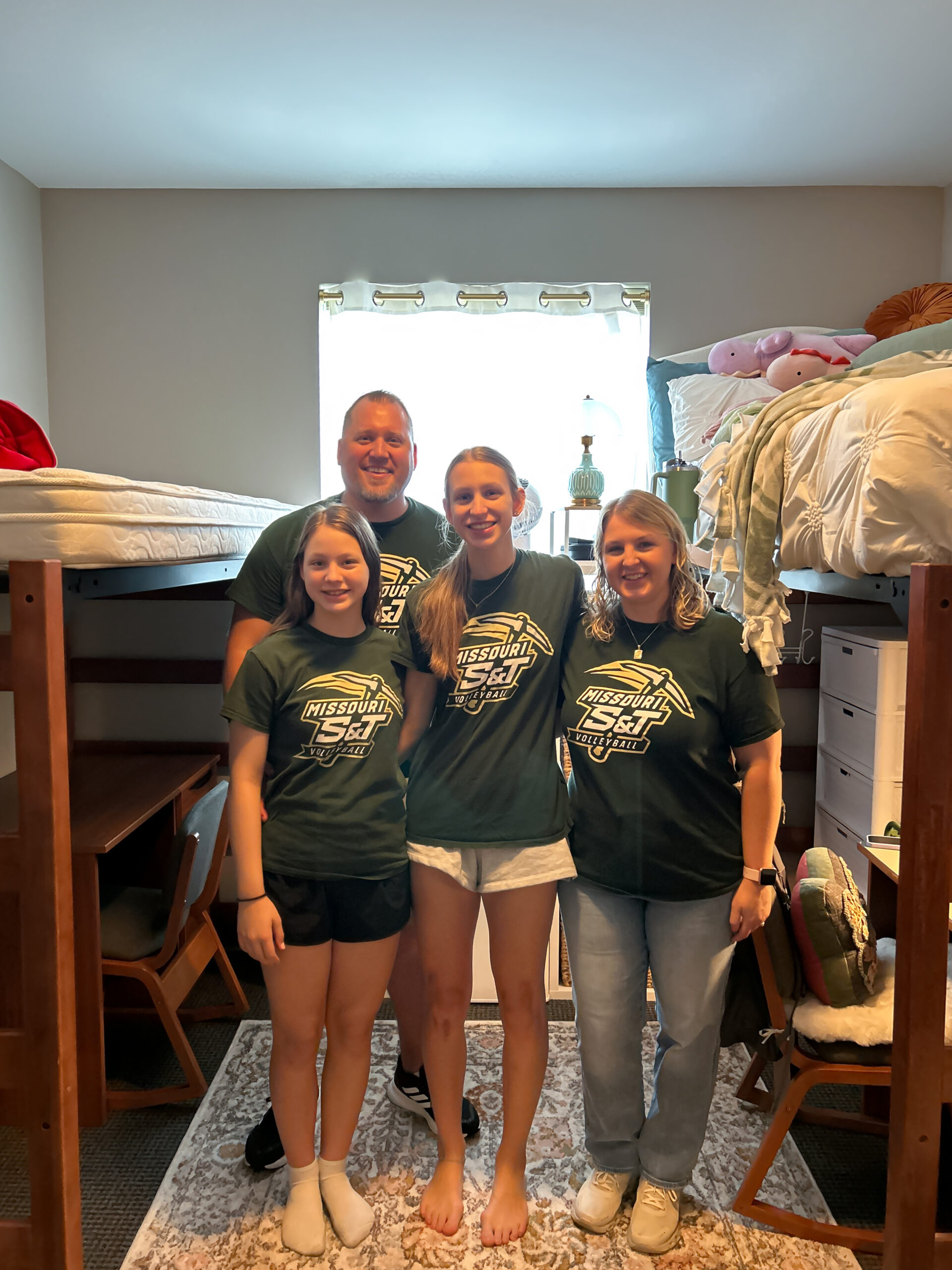 Family of four wearing matching Missouri S&T volleyball shirts in their daughter’s college bedroom on move-in day.