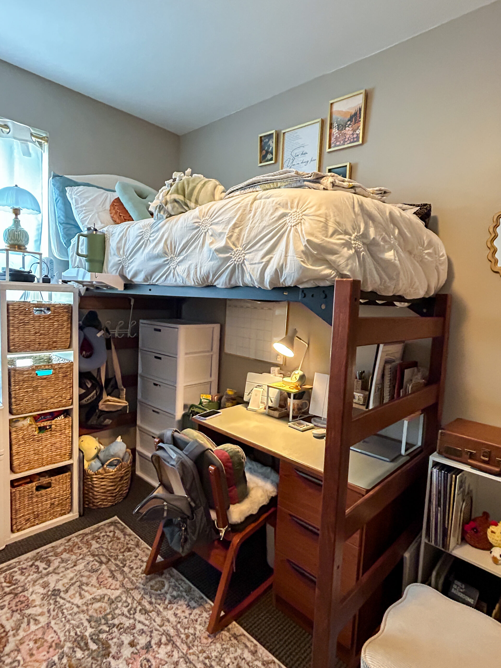 Lofted college bed with white bedding with a desk and storage underneath, surrounded by baskets and organizers for maximizing a small bedroom.