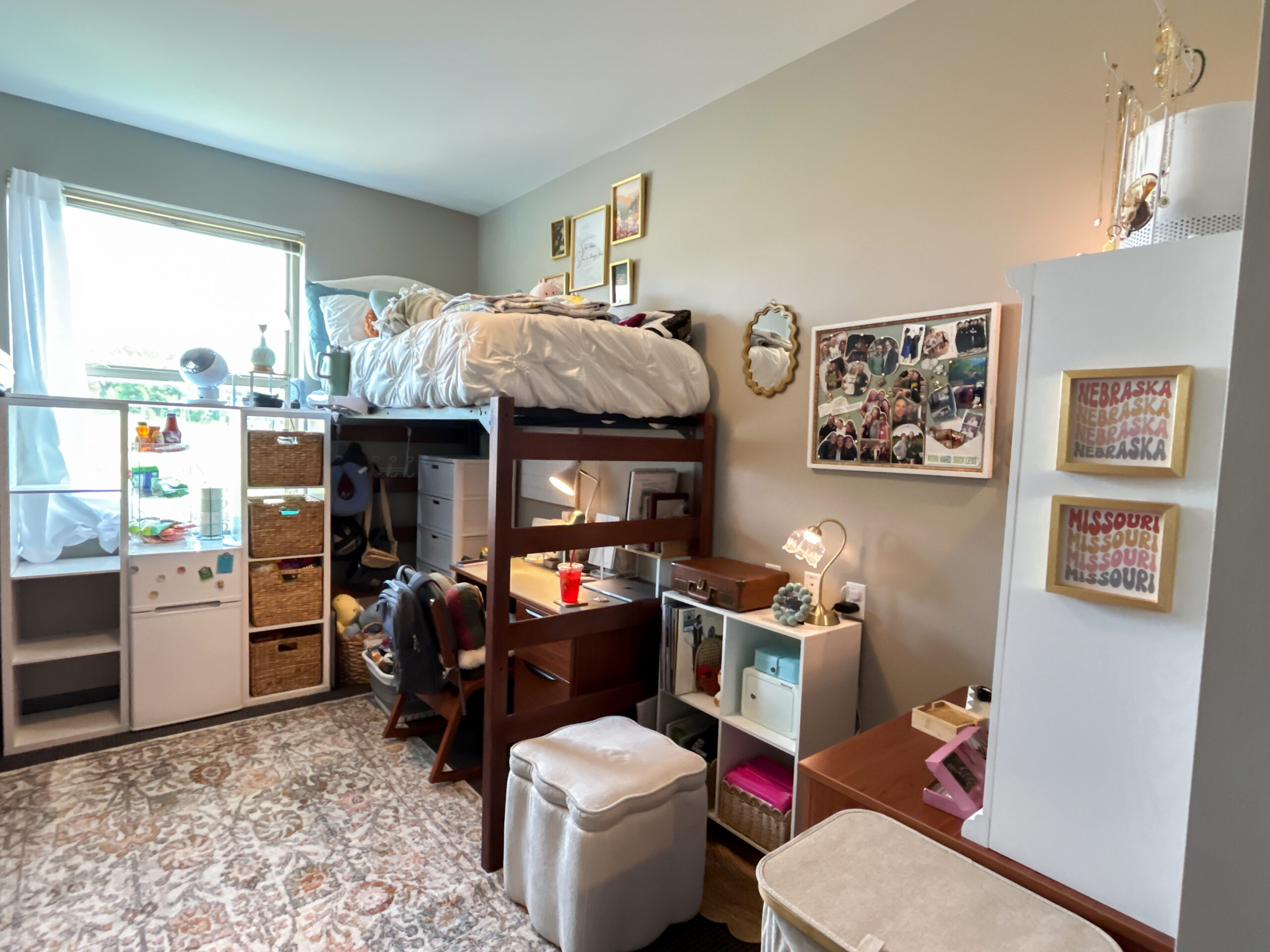 Girl's cozy neutral boho college dorm bedroom decorated with a lofted bed, desk, storage cubes, woven baskets, rug, and personal photos.