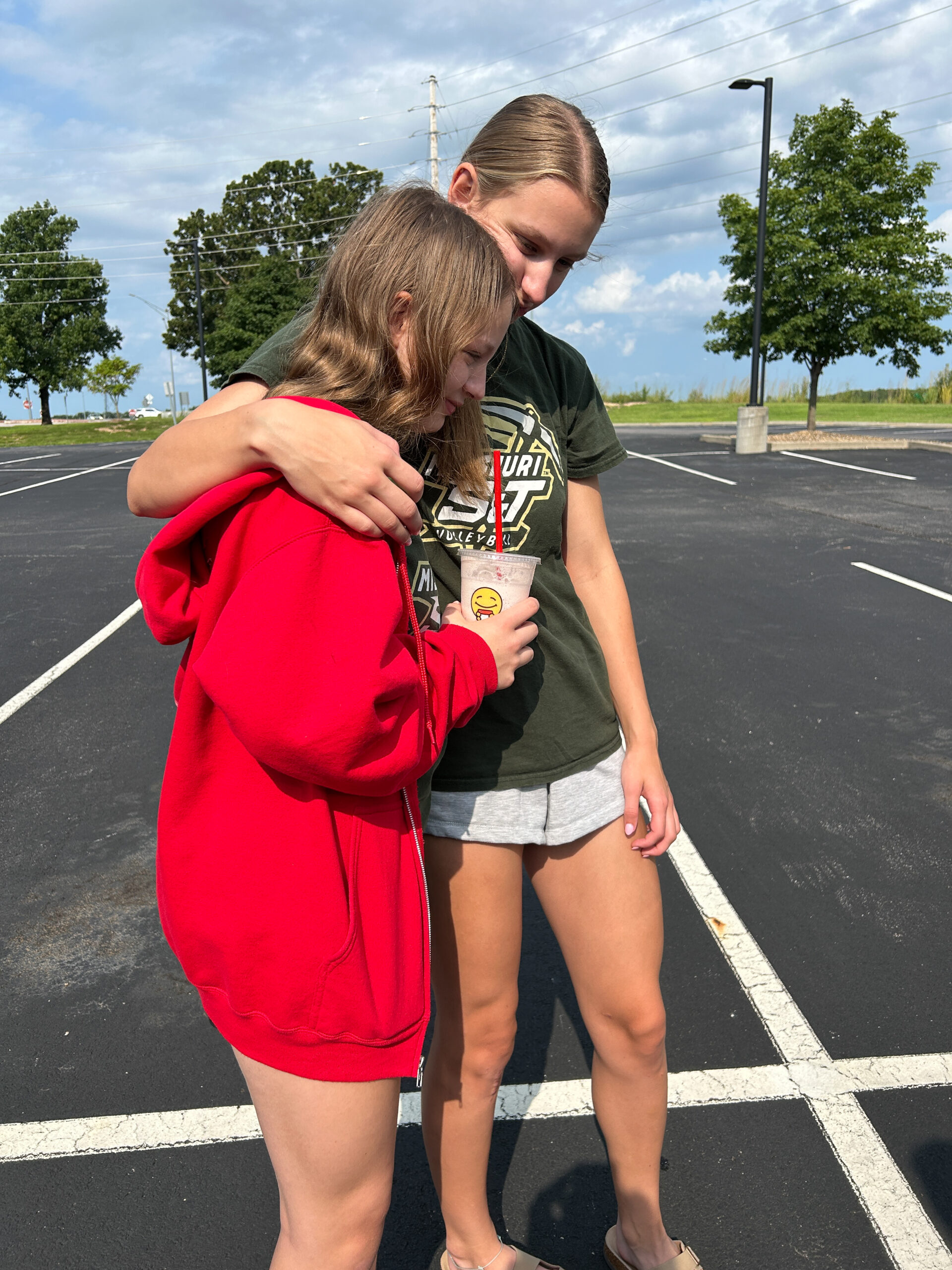 Older sister hugs her younger sister goodbye in a parking lot after college move-in.
