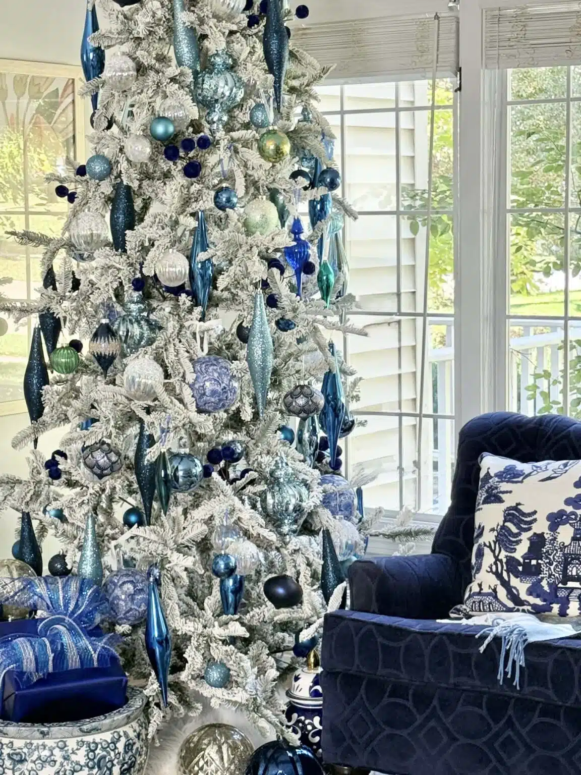 Blue and silver holiday color palette on a flocked Christmas tree decorated with blue and silver ornaments, ribbon, and warm white lights.