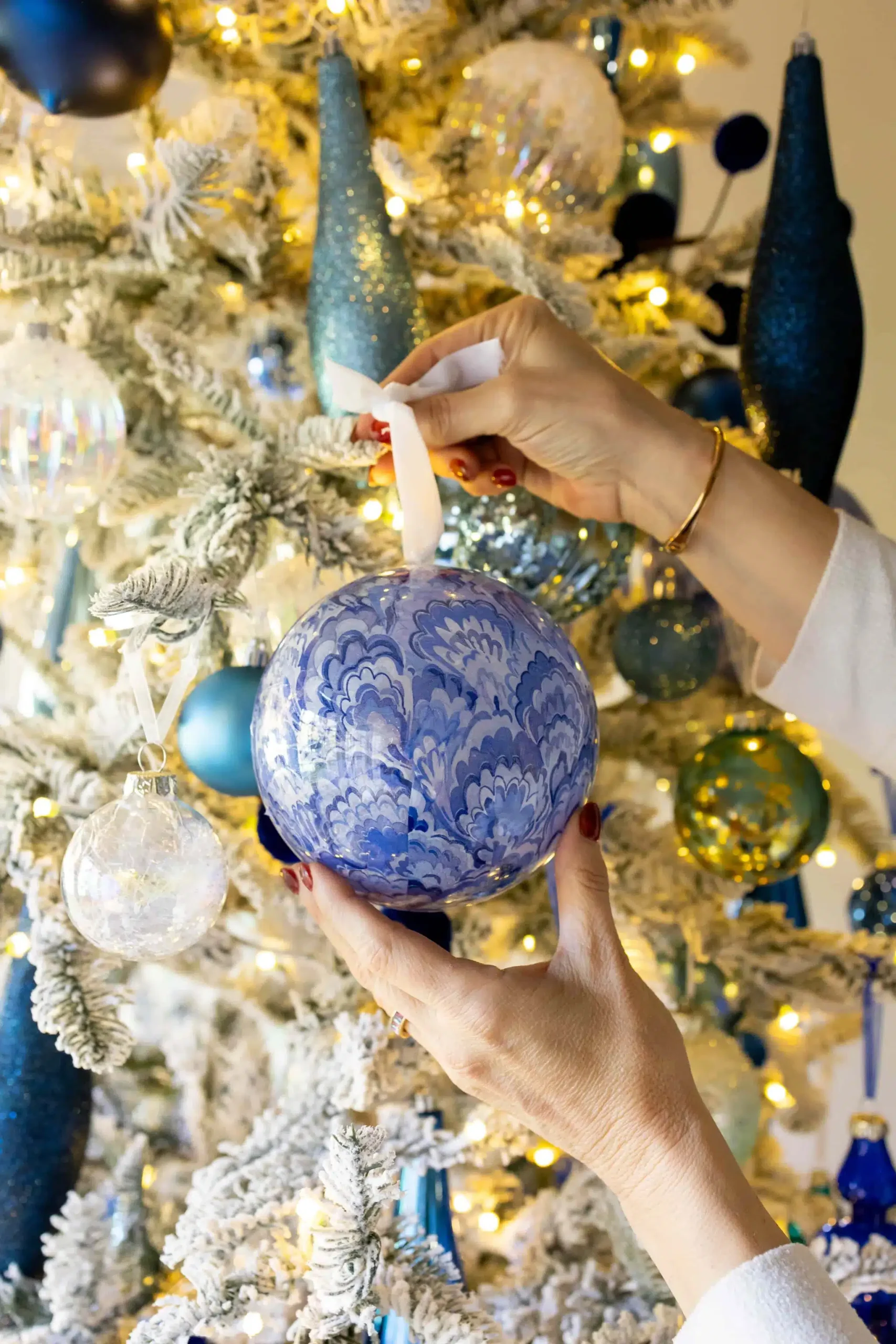 Blue and silver Christmas decor with a blue patterned ornament on a flocked tree filled with blue and silver ornaments and twinkle lights.