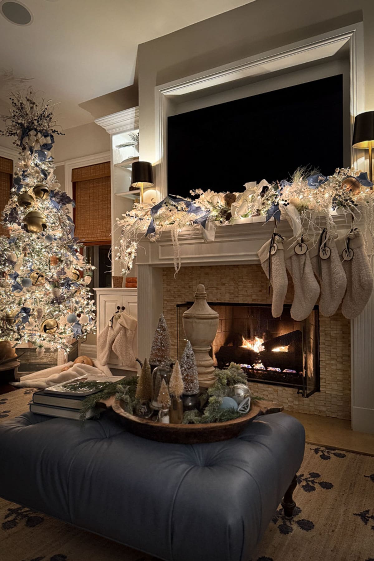 Blue and white Christmas color palette in a living room with a decorated tree, lighted mantel greenery, white stockings, and blue ribbon.