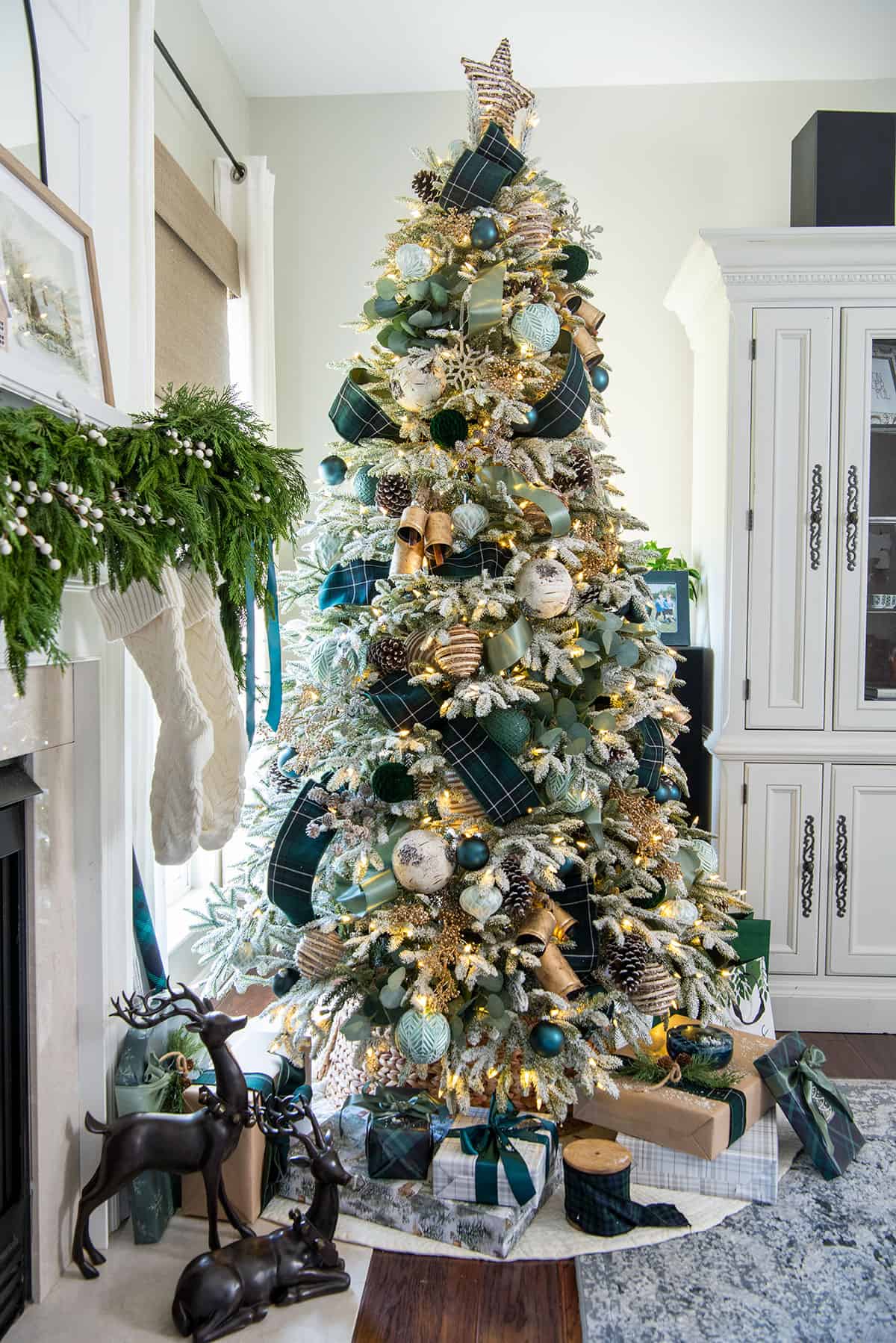 Green and gold holiday color palette on a flocked Christmas tree with dark green, seafoam, and cream ornaments, tartan ribbon, and gold bells.