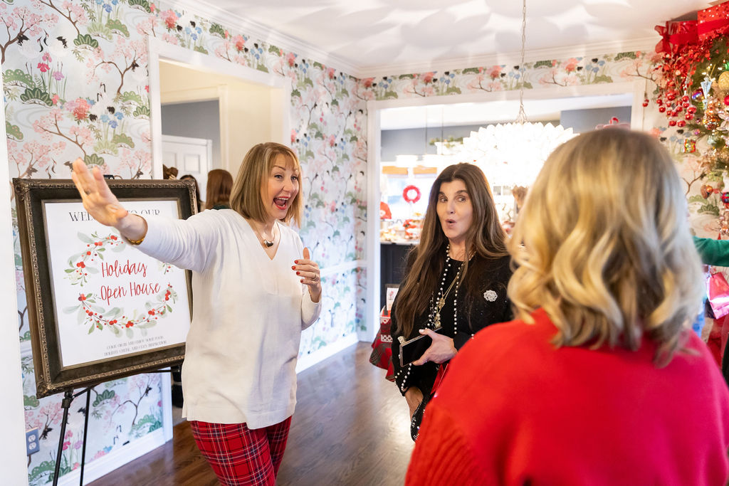 Guests chatting at a festive Holiday Open House beside a decorated Christmas tree and event welcome sign.