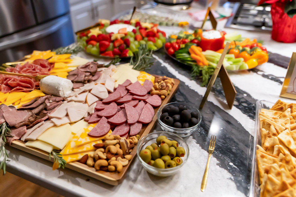 Christmas appetizer spread with a meat and cheese charcuterie board, fruit wreath, fresh vegetables, dips, and crackers.