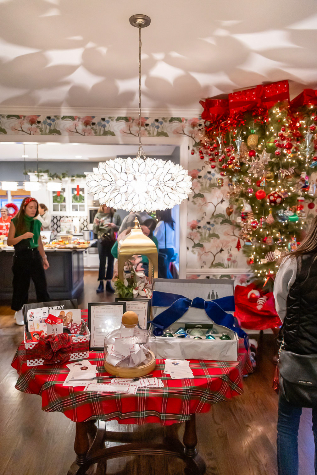 Holiday Open House giveaway table covered in red plaid with prizes and gifts displayed beside a decorated Christmas tree.