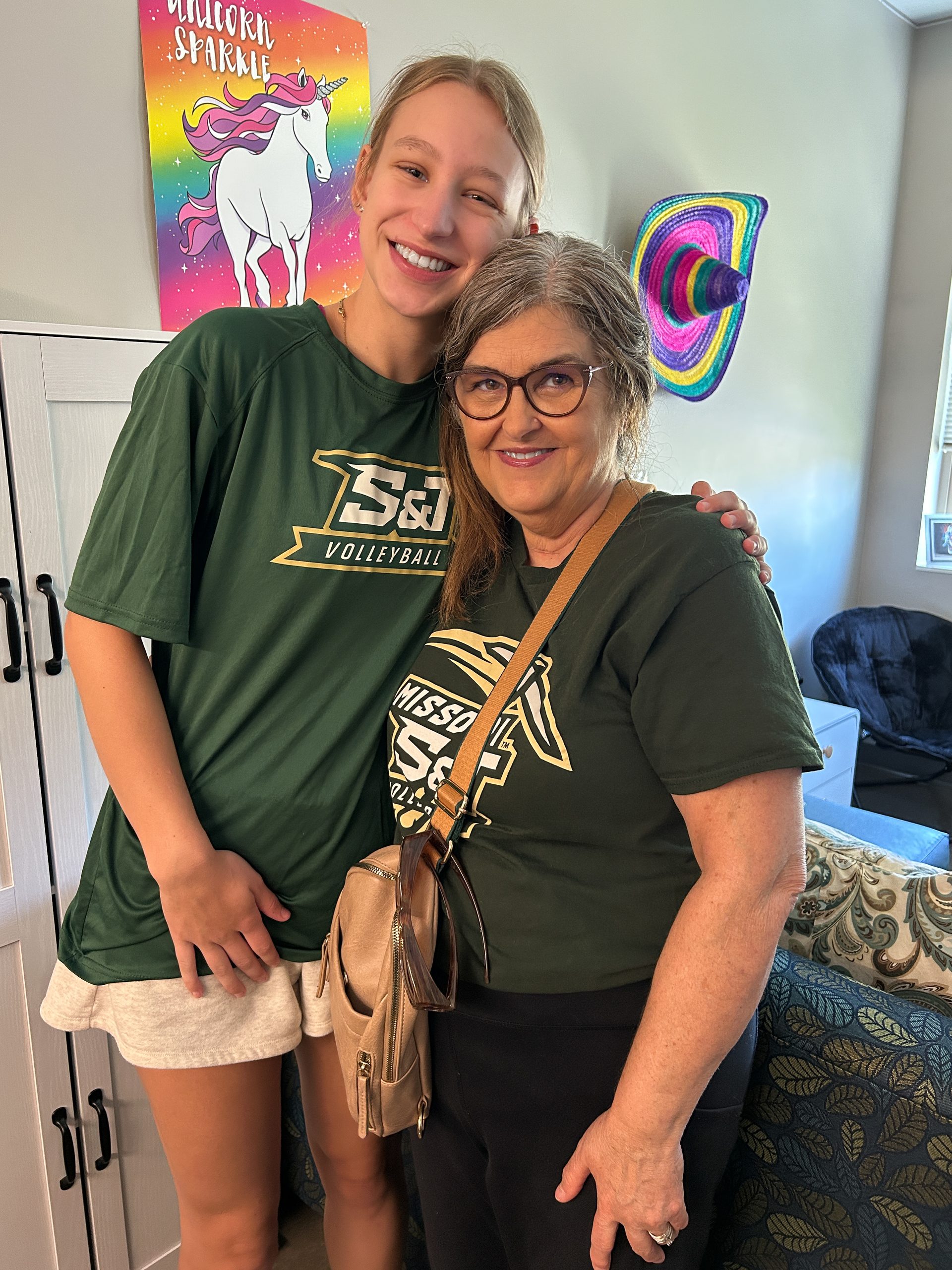 College volleyball player smiling with her grandmother while wearing matching green Missouri S&T shirts.