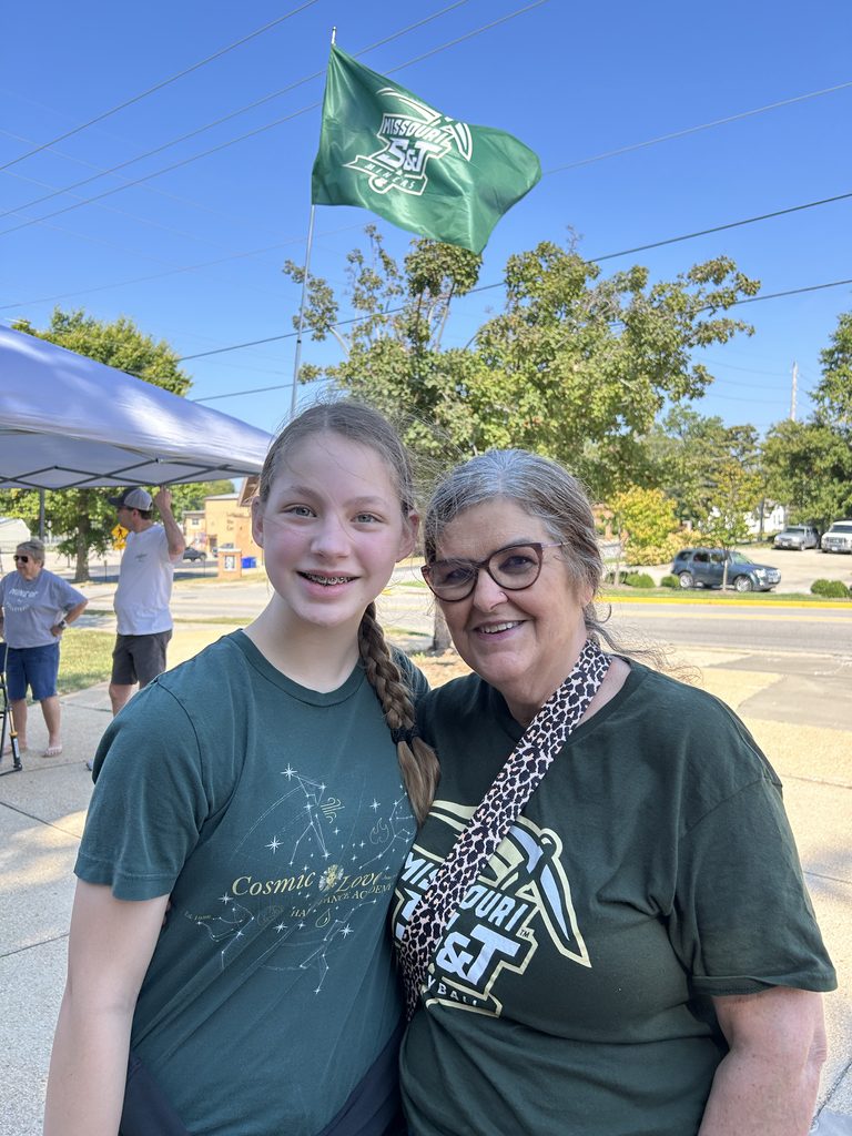 Grandmother and granddaughter at a Missouri S&T volleyball tailgate with a Miners flag flying behind them.