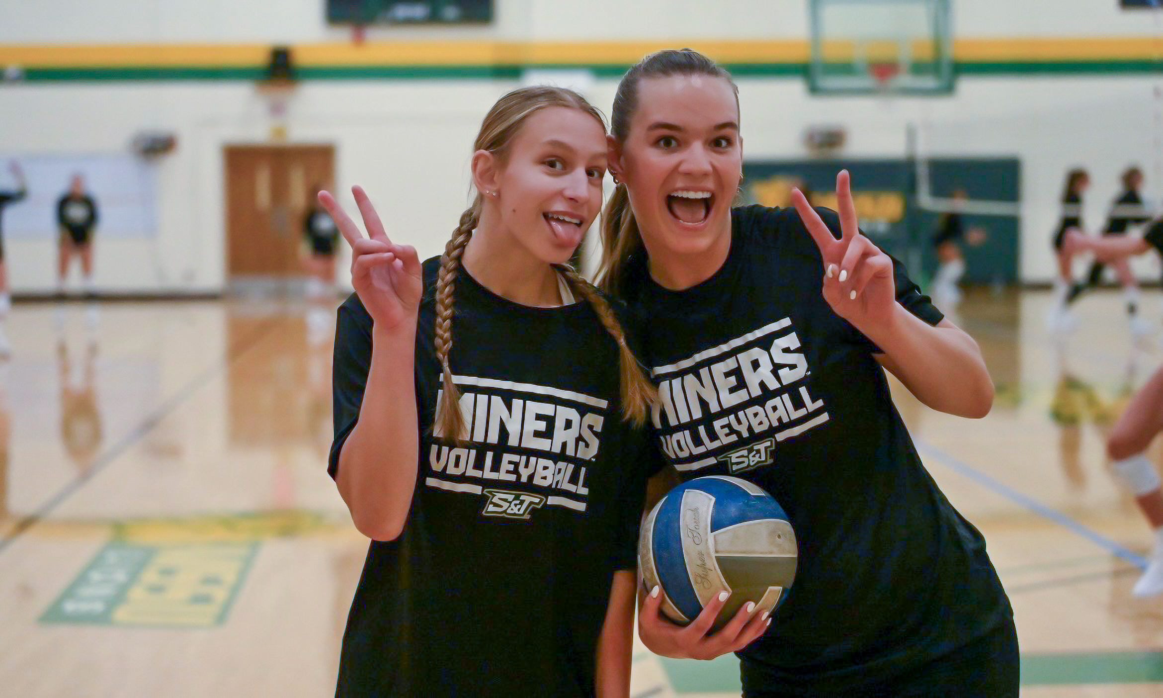 Missouri S&T volleyball player posing with a coach holding a volleyball on the court.