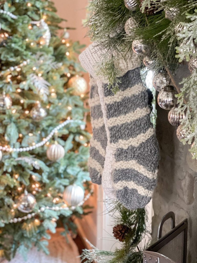 Silver and white Christmas decor with knit stockings, silver ornaments, frosted greenery, and a Christmas tree with silver and white decorations.