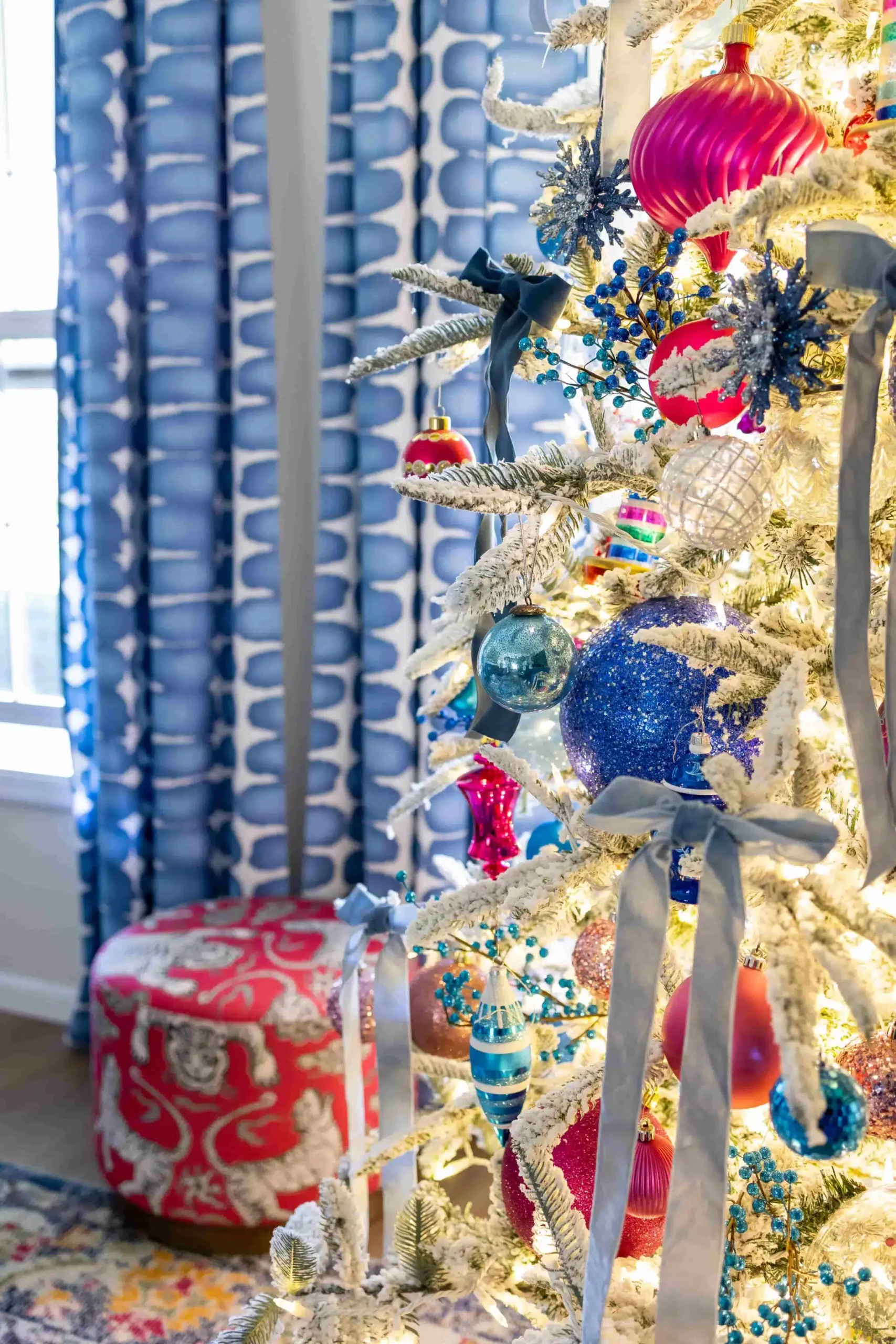 Blue and pink holiday color palette on a flocked Christmas tree with colorful ornaments, blue velvet bows, and twinkle lights.