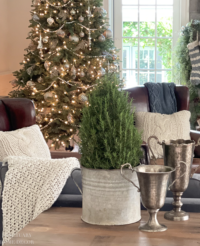 Silver and white Christmas tree decorated with metallic ornaments, beaded garland, and warm white lights beside vintage silver decor.