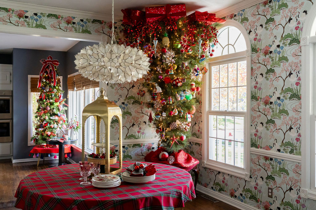 Christmas party table covered in red plaid with stacked plates, festive napkins, glassware, and a gold lantern beside a decorated Christmas tree.