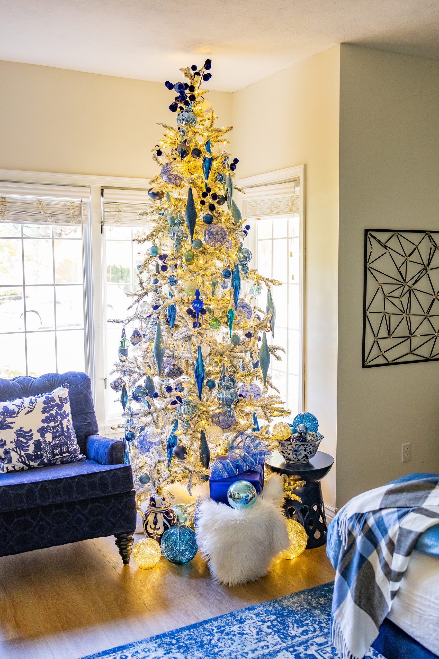 Blue and silver holiday color palette on a flocked Christmas tree decorated with blue and silver ornaments, ribbon, and warm white lights.