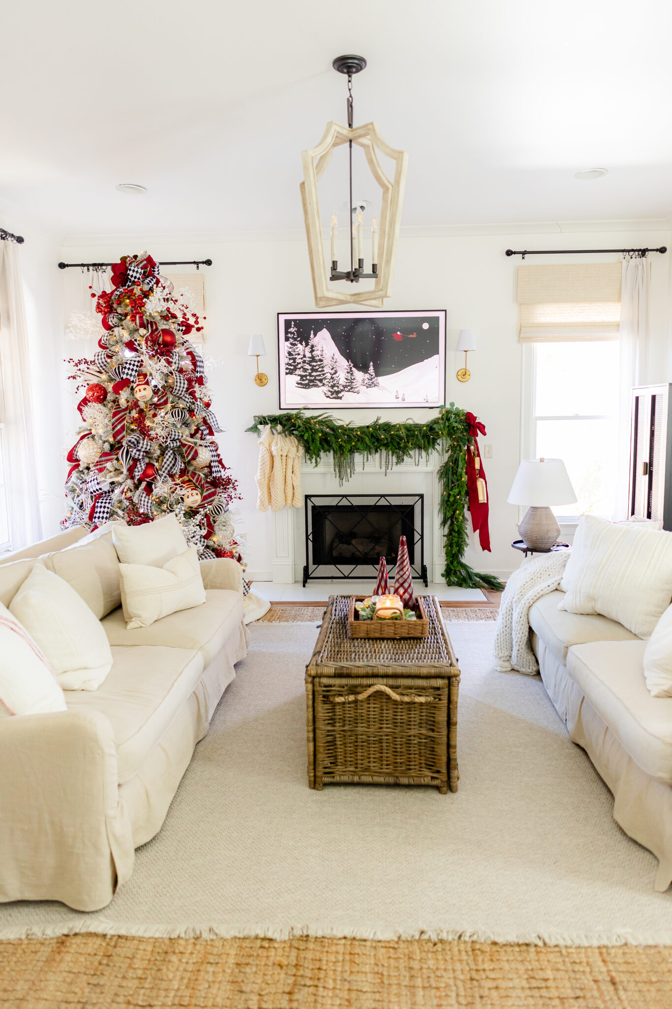 Bright Christmas living room with a red, white, and black decorated Christmas tree and a fireplace mantel draped with greenery and red ribbon.