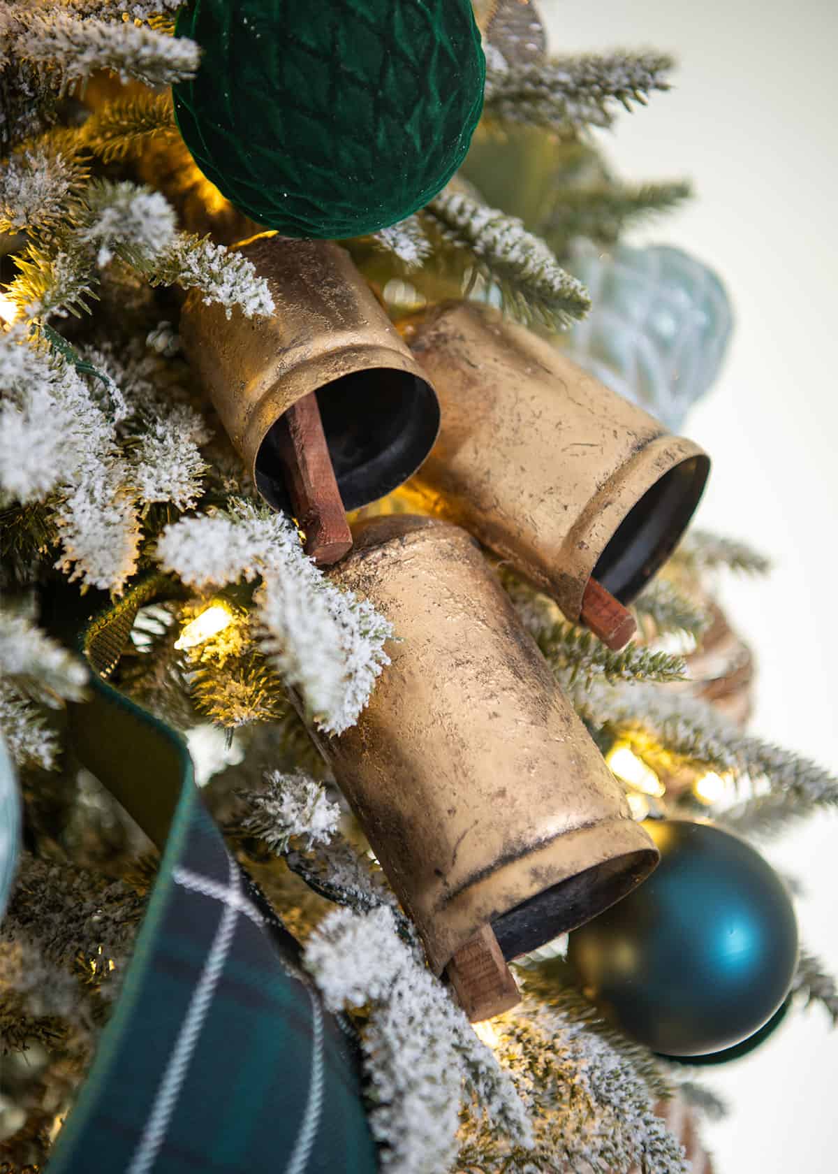 Antique gold bells on a flocked Christmas tree with dark green velvet ornaments, tartan ribbon, and seafoam accents.