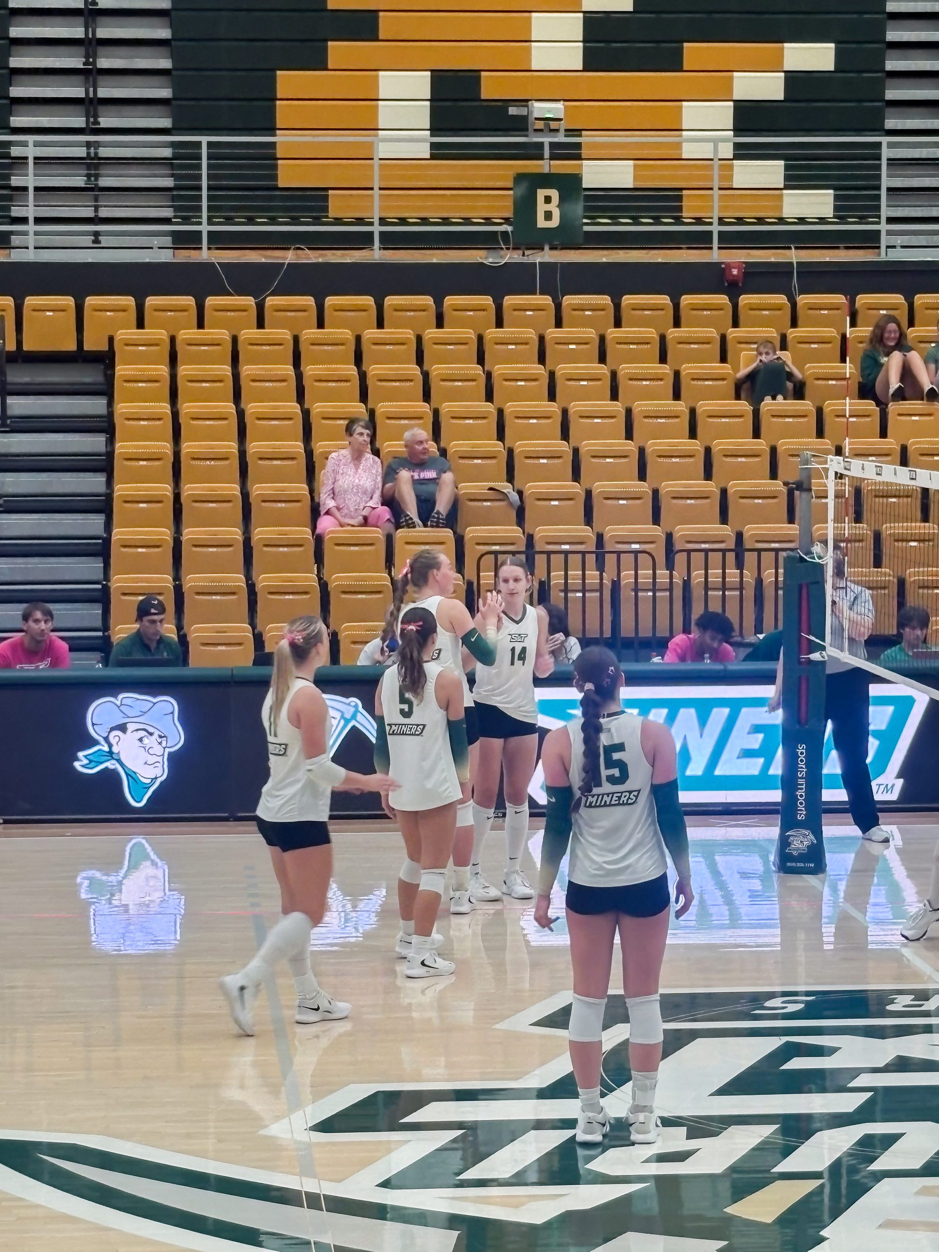 Missouri S&T women's volleyball players stand near the net during a match, with teammates communicating on the court.