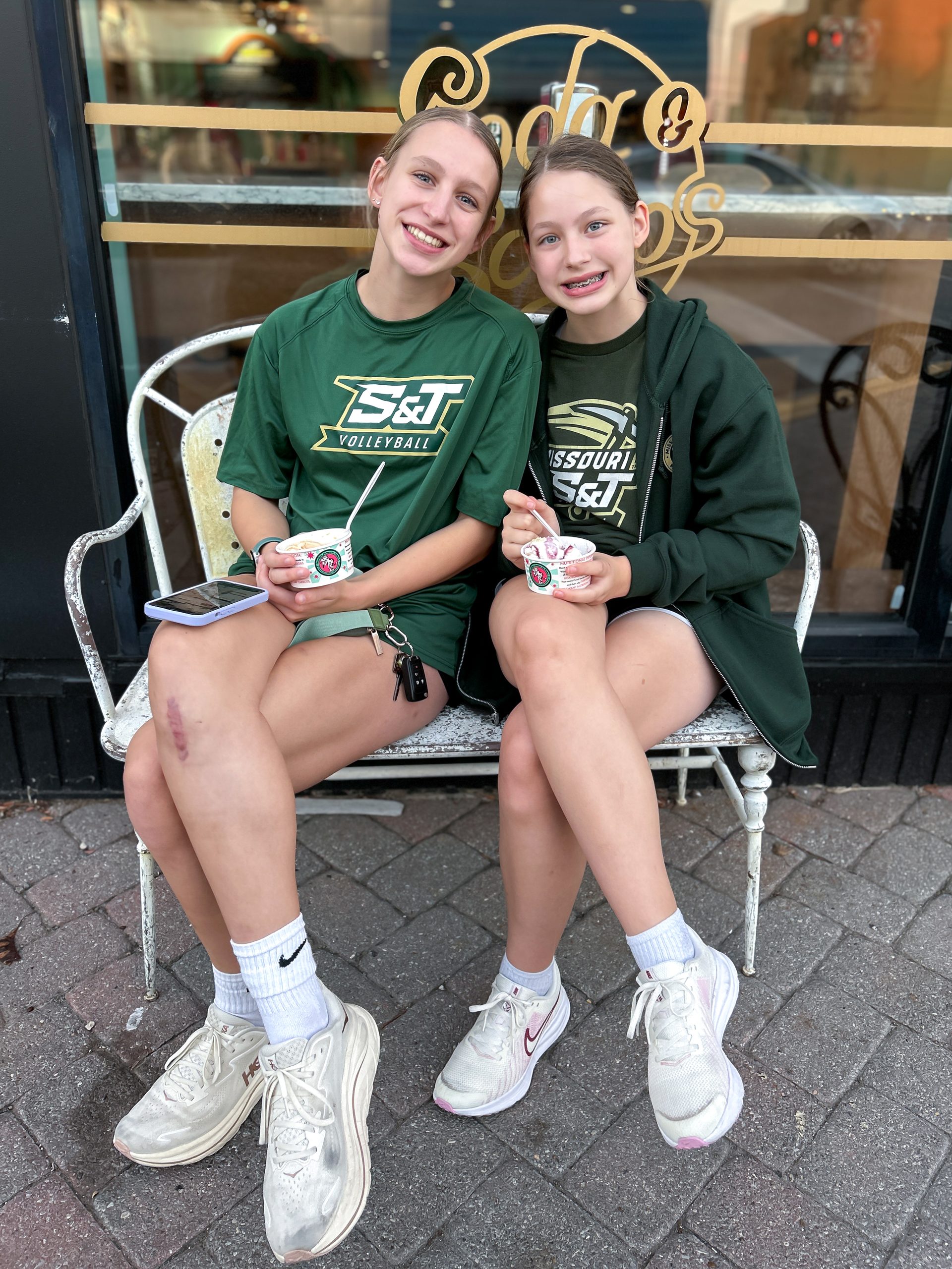 Two sisters wearing green Missouri S&T apparel enjoy ice cream outside Soda and Scoops in Rolla, Missouri.